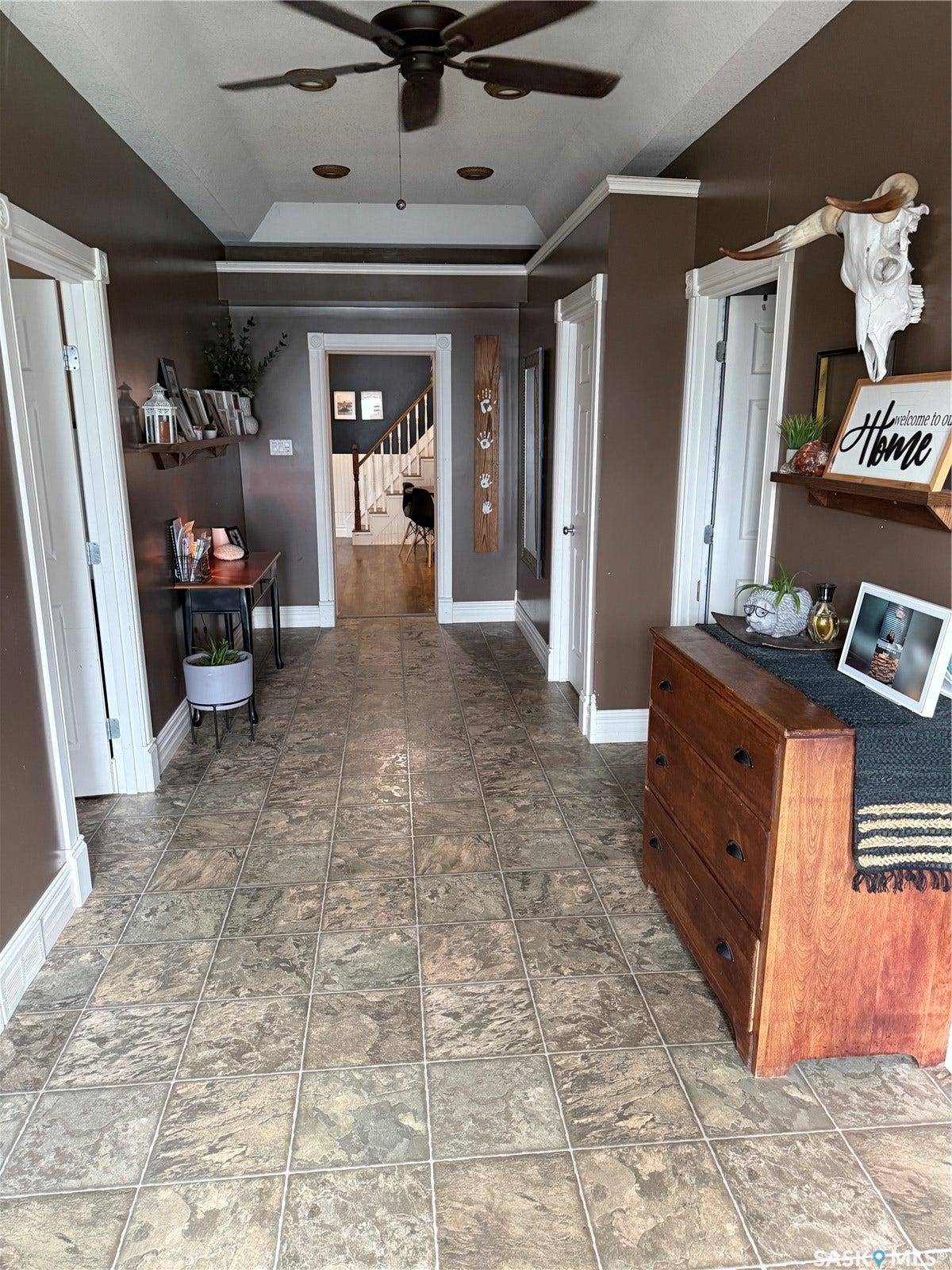 Tray ceiling with recessed lighting, brown ceiling fan, textured tile flooring, and white trim accents