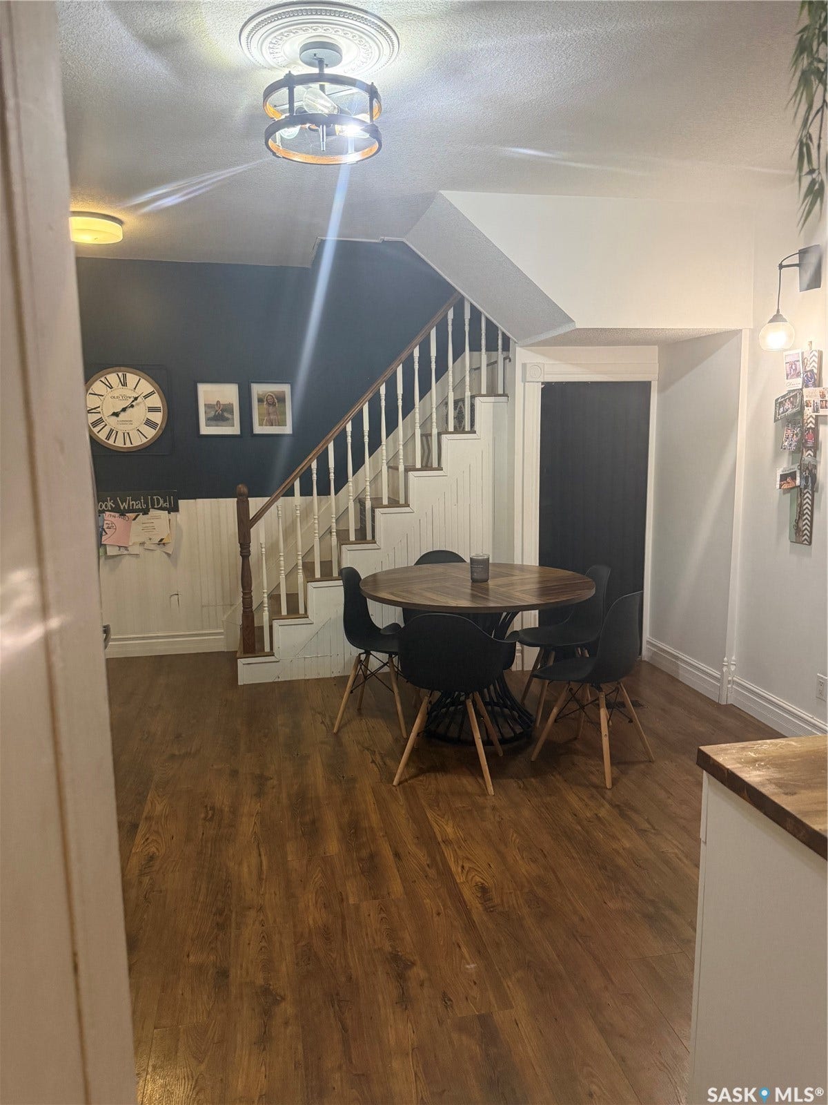 Wood-finish flooring throughout, featuring a staircase with white risers and wooden handrails, and a modern ceiling light fixture with a decorative ceiling medallion