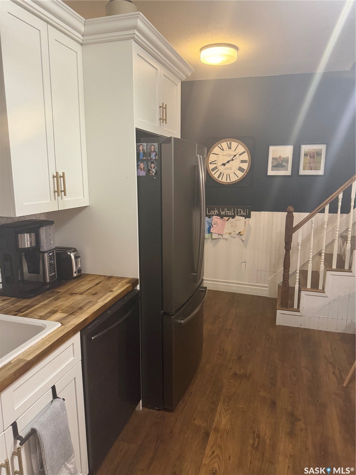 White shaker-style cabinetry with gold-finish hardware, wood-finish countertops, stainless steel appliances, and wood-finish flooring