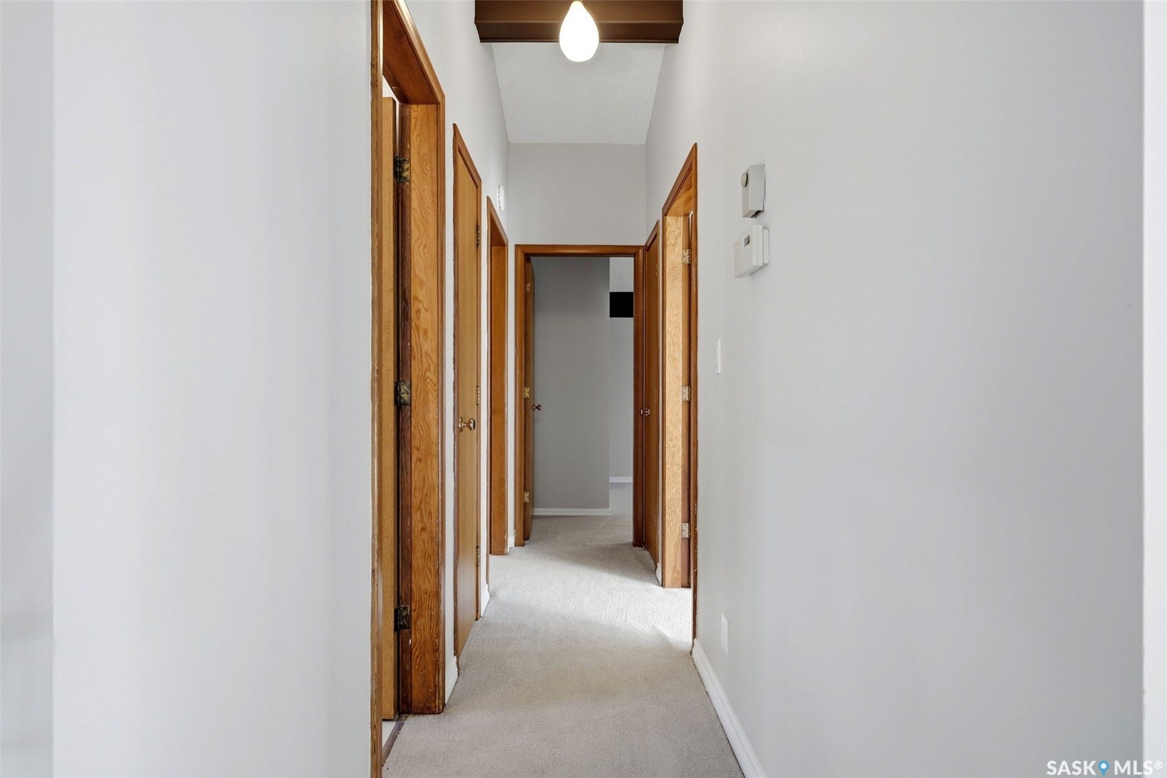 3361 Wascana Street, Regina SK S4S 2H2 Carpeted hallway with light gray walls, multiple wood-finish doors, and a wood-beamed ceiling