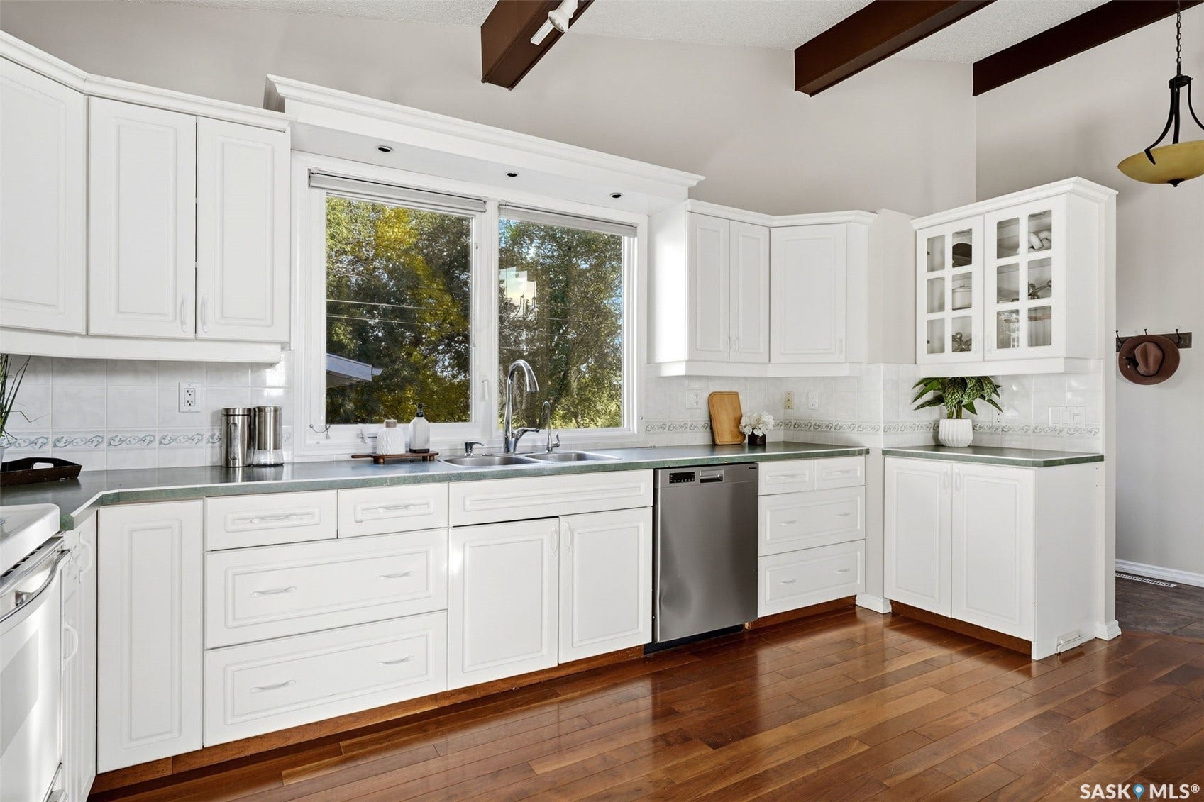 3361 Wascana Street, Regina SK S4S 2H2 White cabinetry with paneled doors, stainless steel dishwasher, wood-finish flooring, recessed lighting, and a vaulted ceiling with exposed beams
