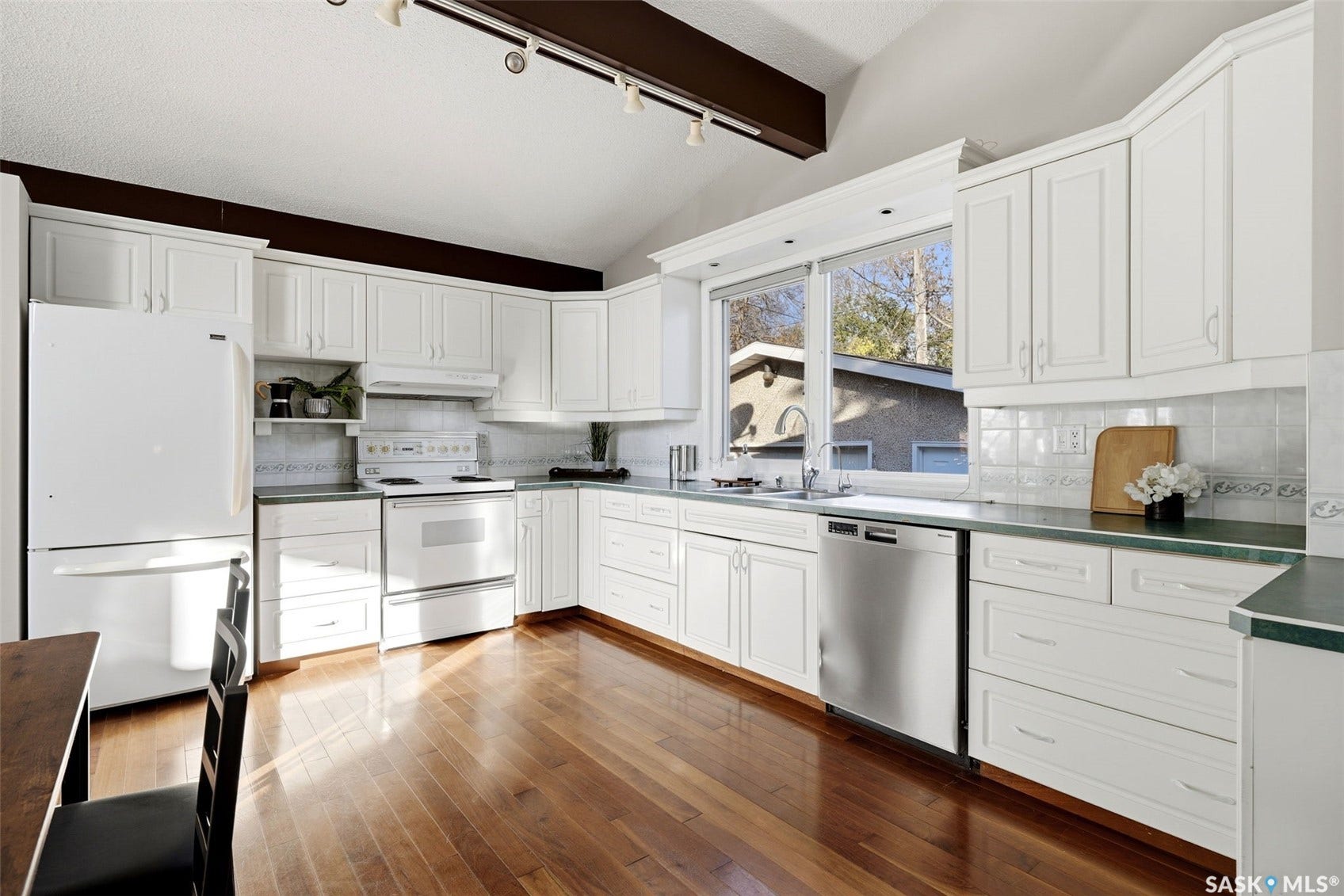 3361 Wascana Street, Regina SK S4S 2H2 Vaulted ceiling with exposed wood beam, wood-finish flooring, white cabinetry, integrated stainless steel dishwasher, and a large window above the sink