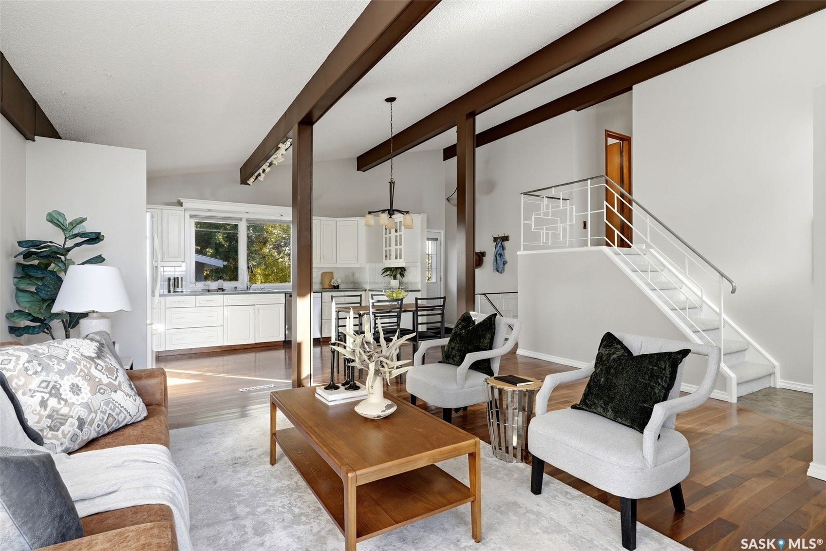 3361 Wascana Street, Regina SK S4S 2H2 Open-concept interior featuring rich wood-finish flooring, exposed ceiling beams, white cabinetry, a modern staircase with decorative railing, and recessed lighting