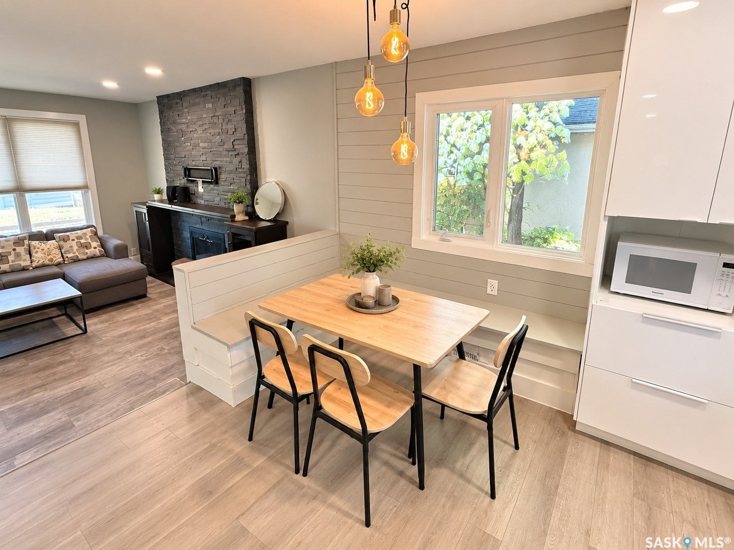 5810 Sherwood Drive, Regina SK S4T 6Y7 Open-concept living space featuring wood-finish flooring, built-in banquette seating, a stacked stone accent wall, and recessed ceiling lighting