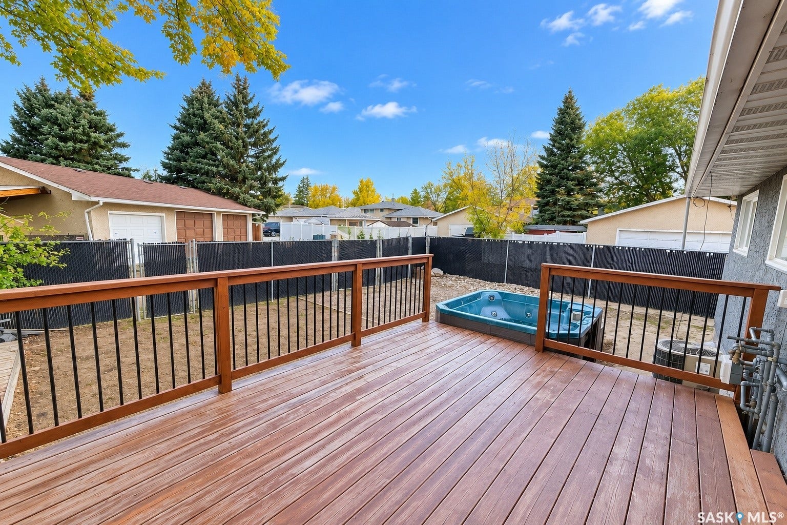 5810 Sherwood Drive, Regina SK S4T 6Y7 Expansive wood-finish deck with a built-in hot tub, durable railings featuring metal balusters, and mature evergreen trees
