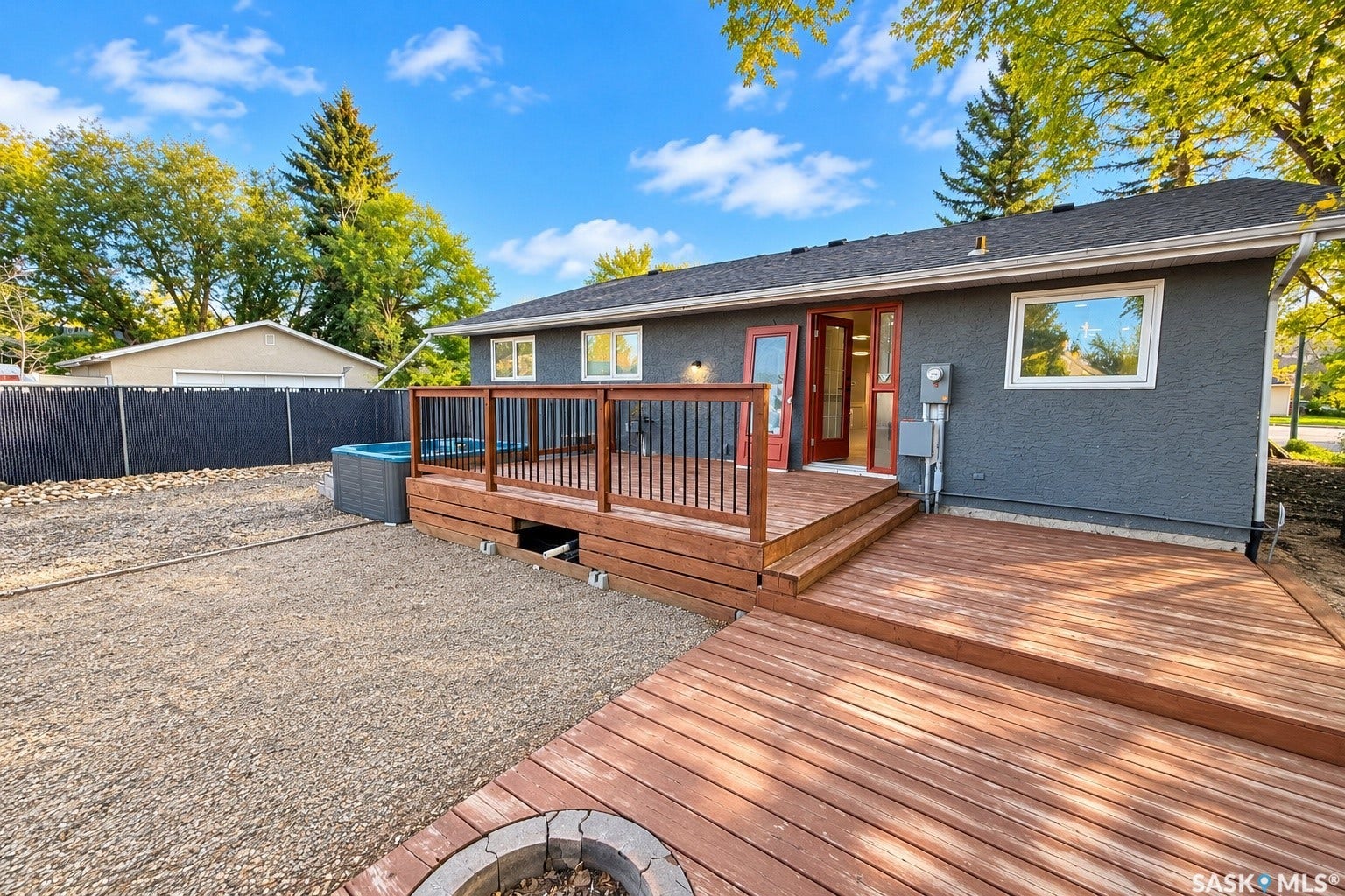 5810 Sherwood Drive, Regina SK S4T 6Y7 Multi-level wood deck with black metal railings, leading to a gravel yard