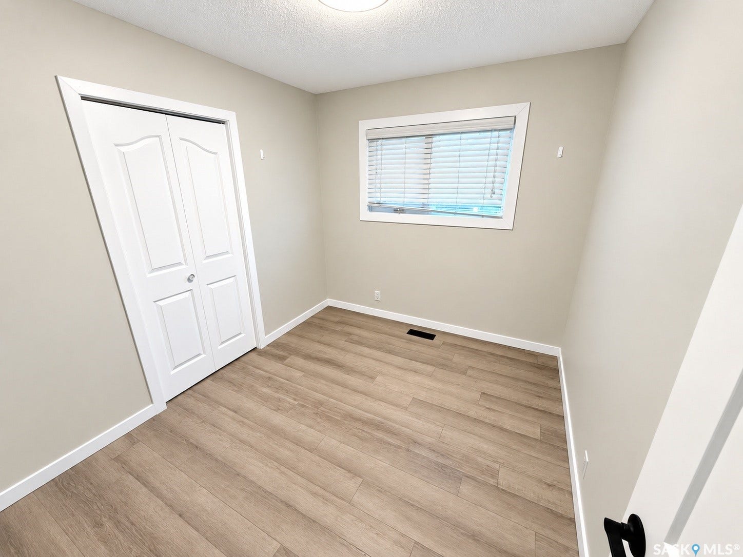 5810 Sherwood Drive, Regina SK S4T 6Y7 Neutral wall paint, wood-finish flooring, white bi-fold closet doors, white window trim, and a ceiling-mounted light fixture