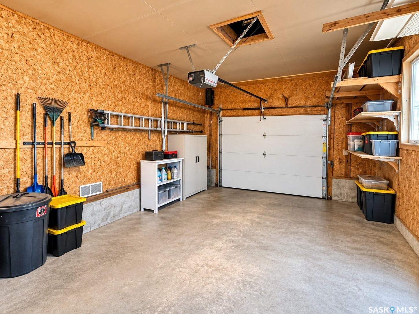 5810 Sherwood Drive, Regina SK S4T 6Y7 Attached garage featuring composite wood paneling, a concrete floor, built-in shelving, and a white overhead door