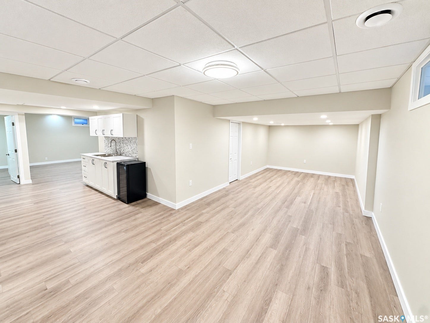 5810 Sherwood Drive, Regina SK S4T 6Y7 Expansive open-concept room featuring wood-finish flooring, recessed lighting, and a built-in wet bar with white cabinetry and a mosaic tile backsplash