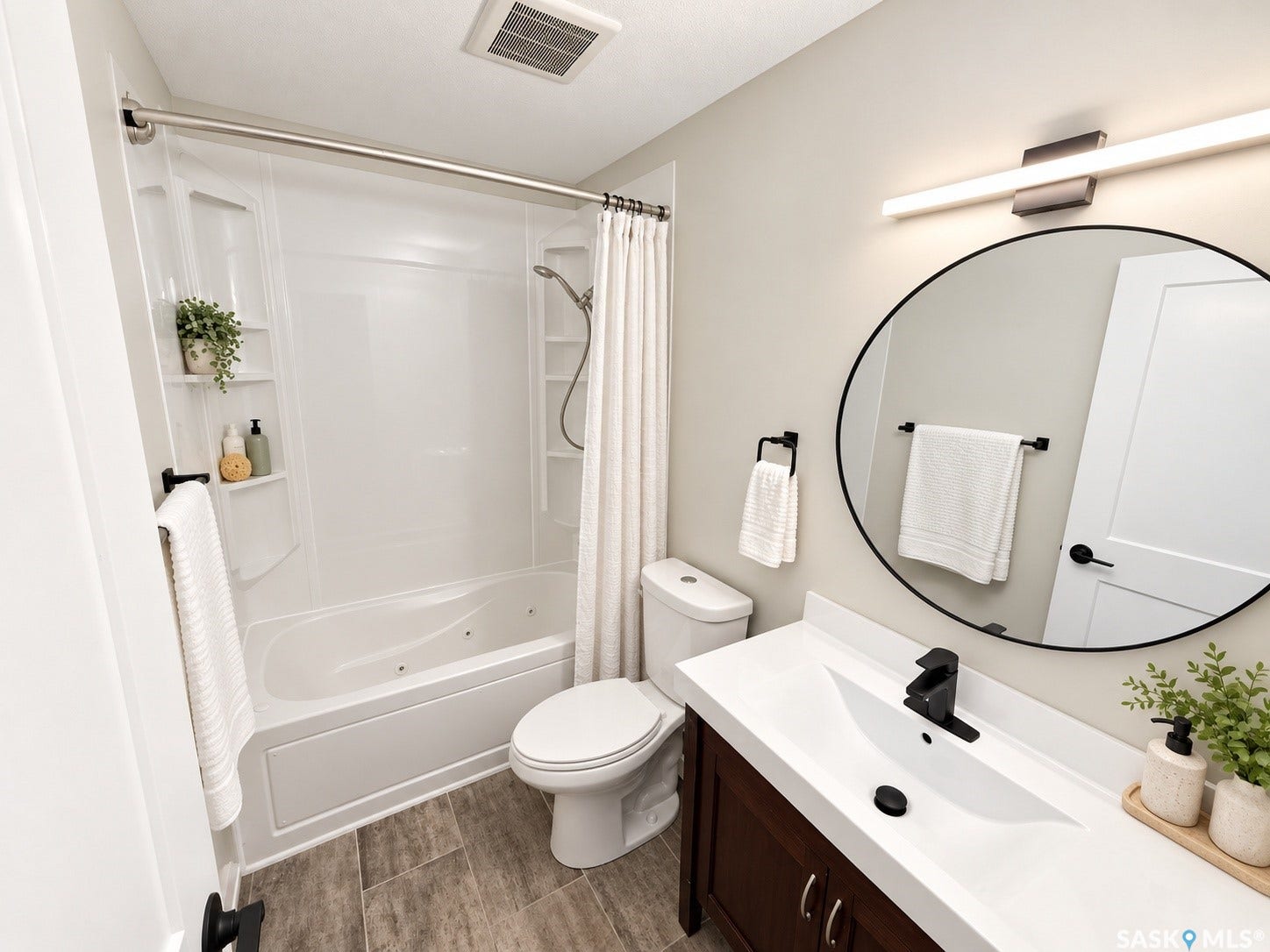 5810 Sherwood Drive, Regina SK S4T 6Y7 White acrylic bathtub with built-in shelving, wood-finish flooring, dark wood vanity with white countertop, integrated sink, and a circular mirror