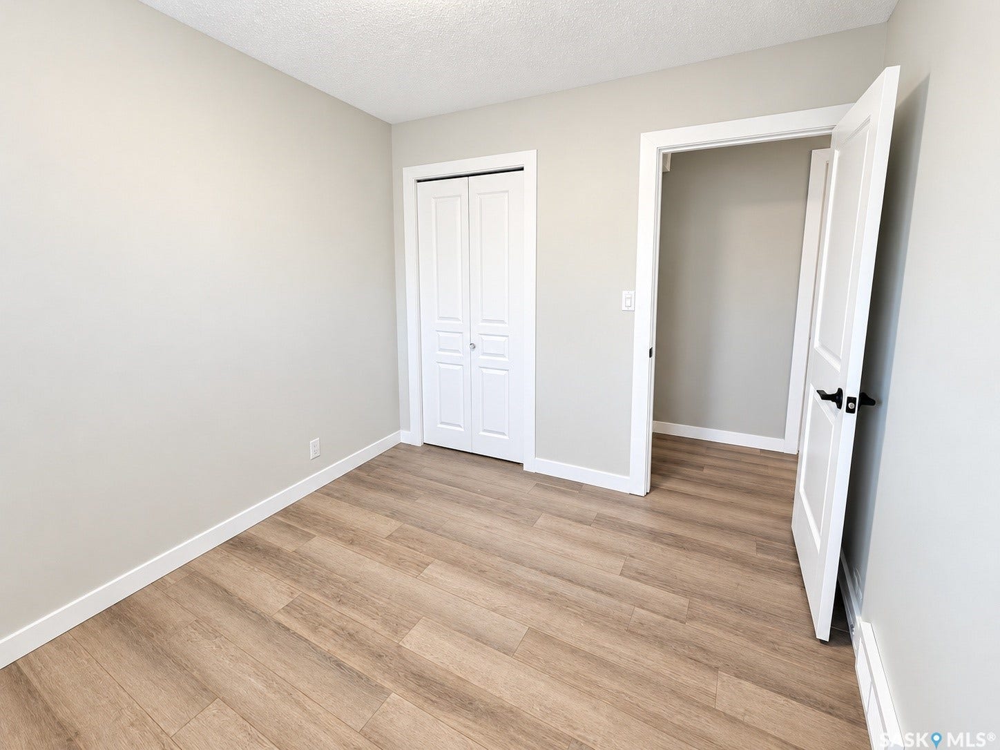 5810 Sherwood Drive, Regina SK S4T 6Y7 Neutral wall tones, wood-finish flooring, white baseboards, white paneled doors, and matte black door hardware