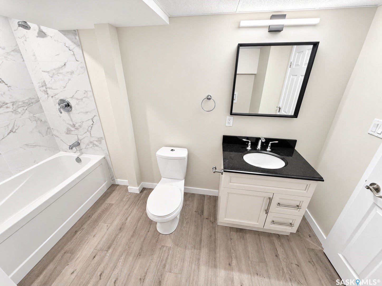 5810 Sherwood Drive, Regina SK S4T 6Y7 Bathroom featuring a white bathtub with marble-look tile surround, wood-finish flooring, and a vanity with a dark countertop and undermount sink