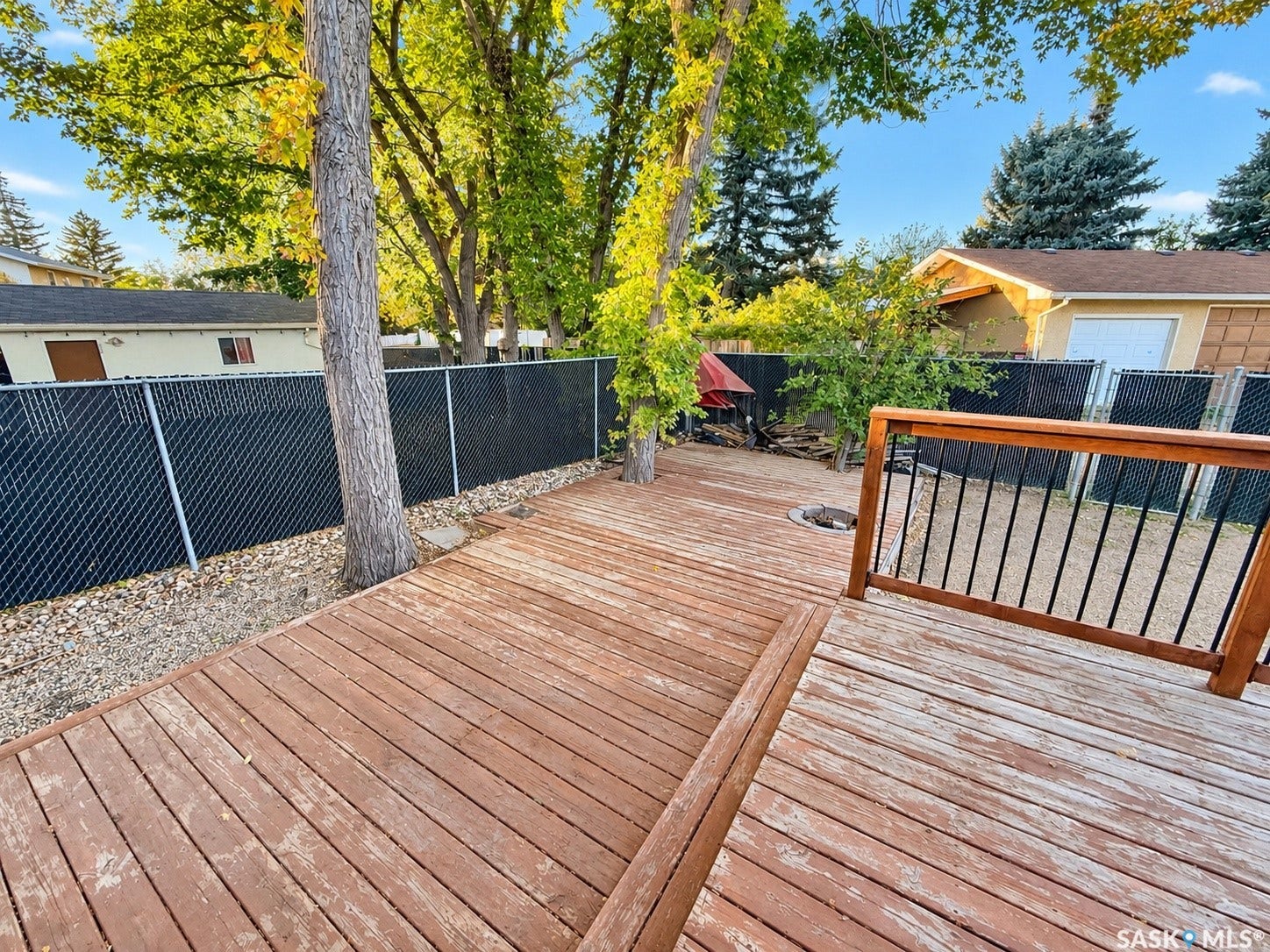 5810 Sherwood Drive, Regina SK S4T 6Y7 Expansive wood decking with a built-in fire pit and black metal chain link fencing