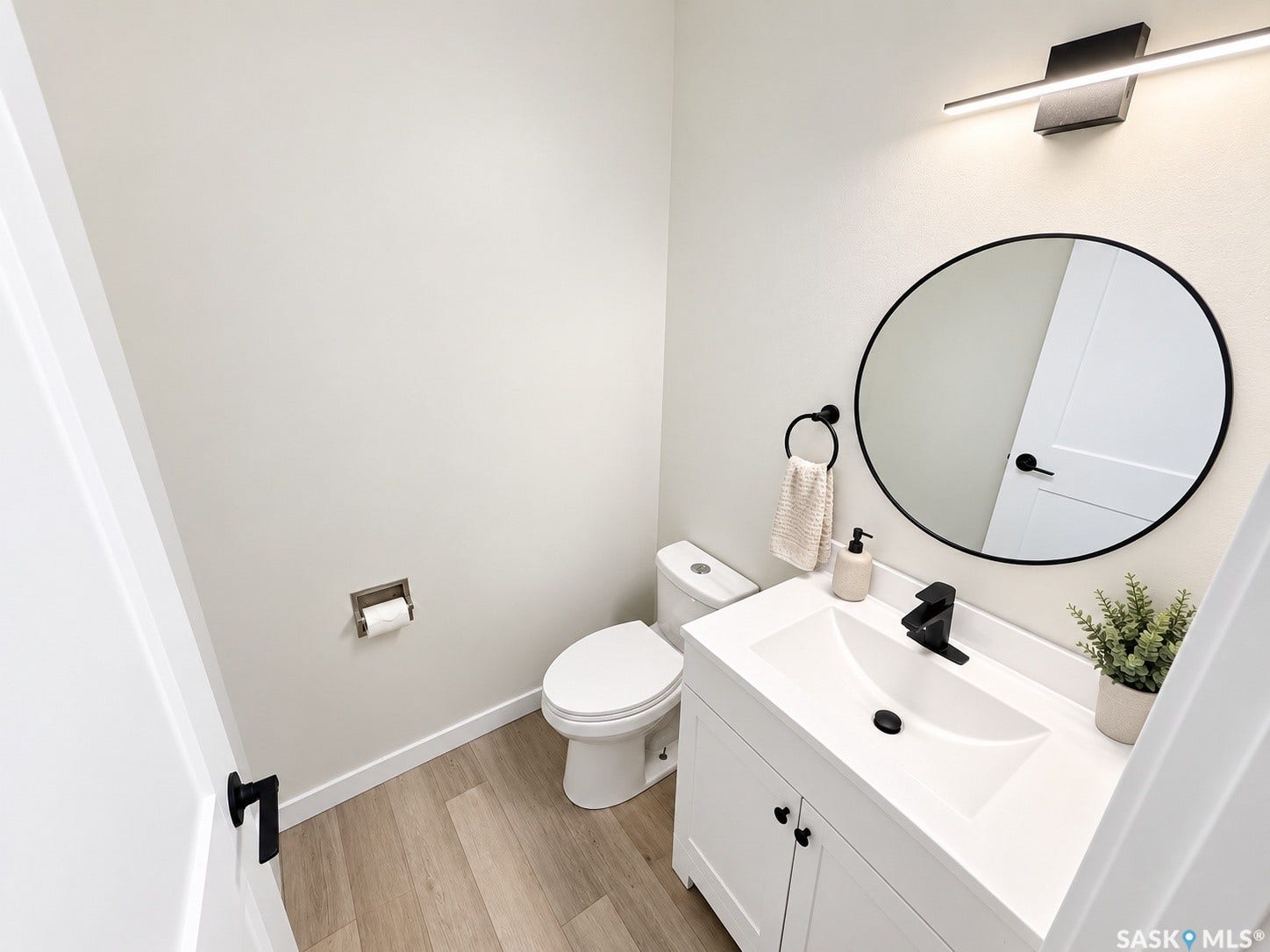 5810 Sherwood Drive, Regina SK S4T 6Y7 White vanity with integrated sink, black single-handle faucet, round black-framed mirror, and wood-finish flooring