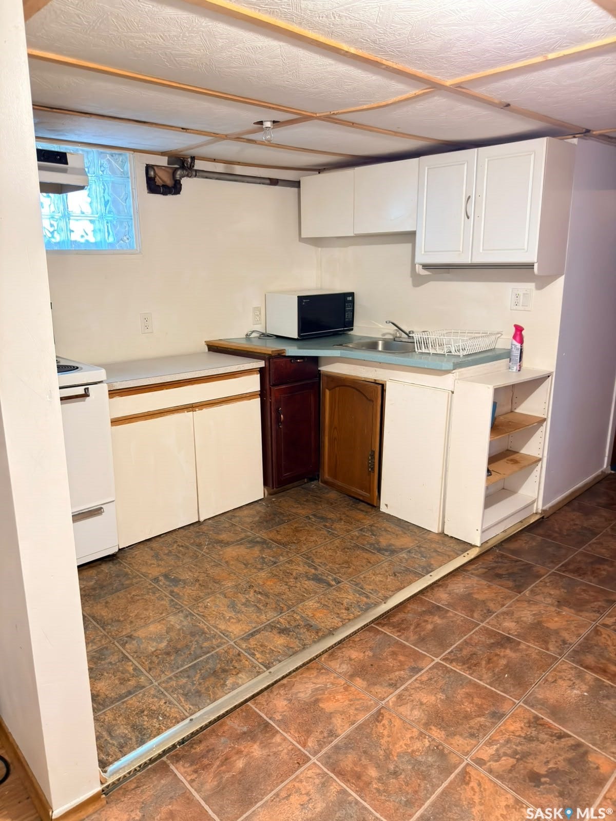 Compact kitchen area featuring white upper and lower cabinetry, a built-in sink, and tile flooring