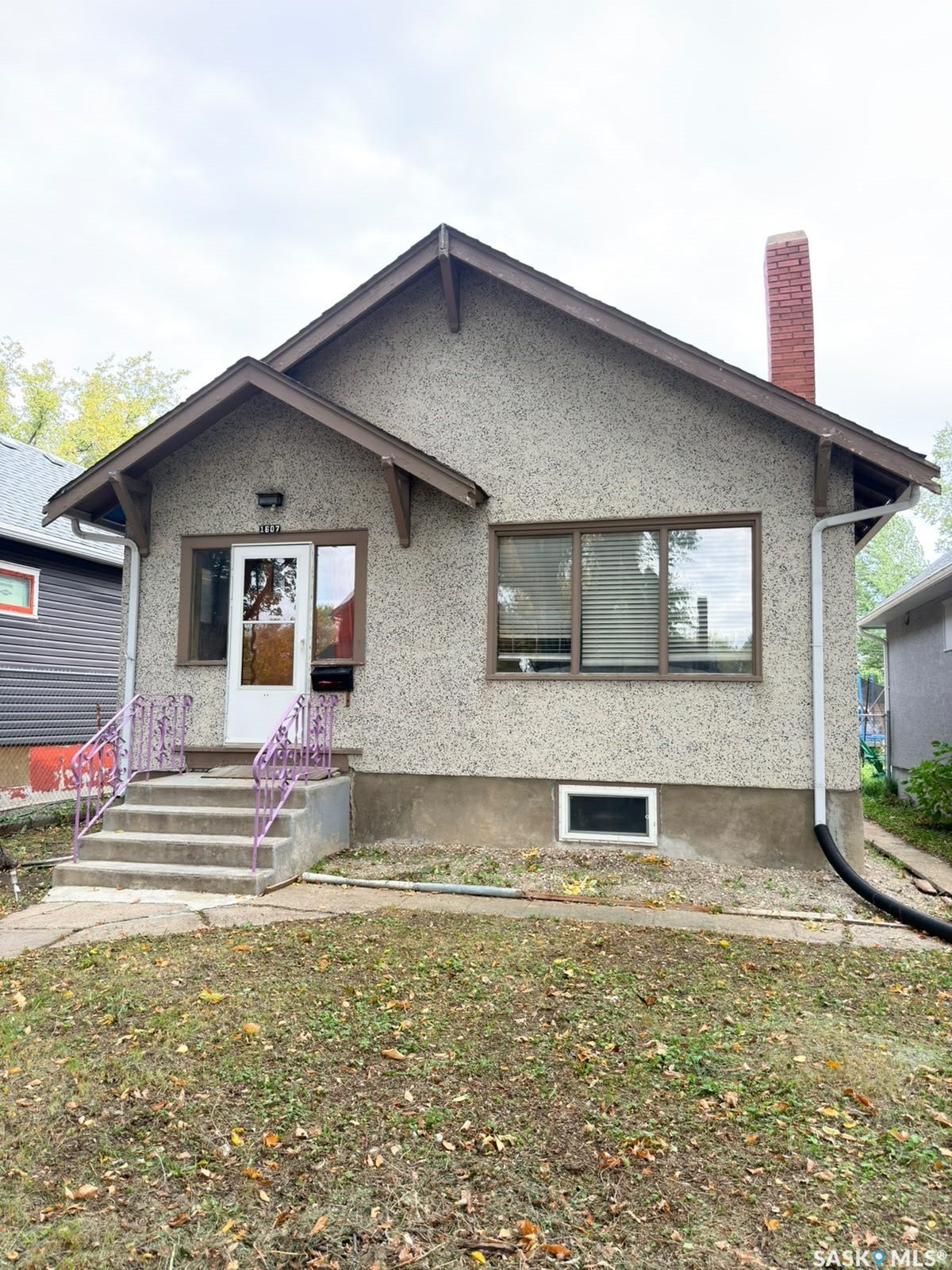 Stucco exterior with a peaked roofline, a brick chimney, and concrete entry steps