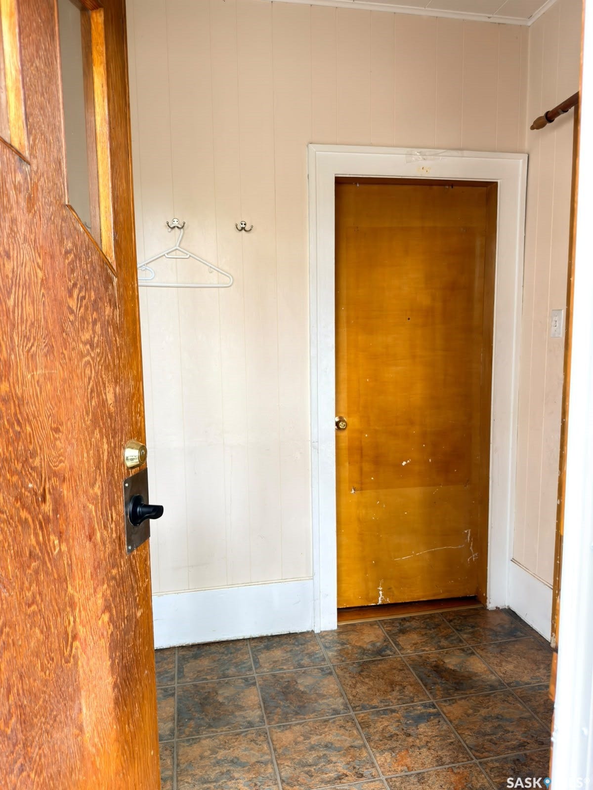 Wood-paneled entry door with dark hardware, leading to a space with paneled walls, white trim, and square-tiled flooring