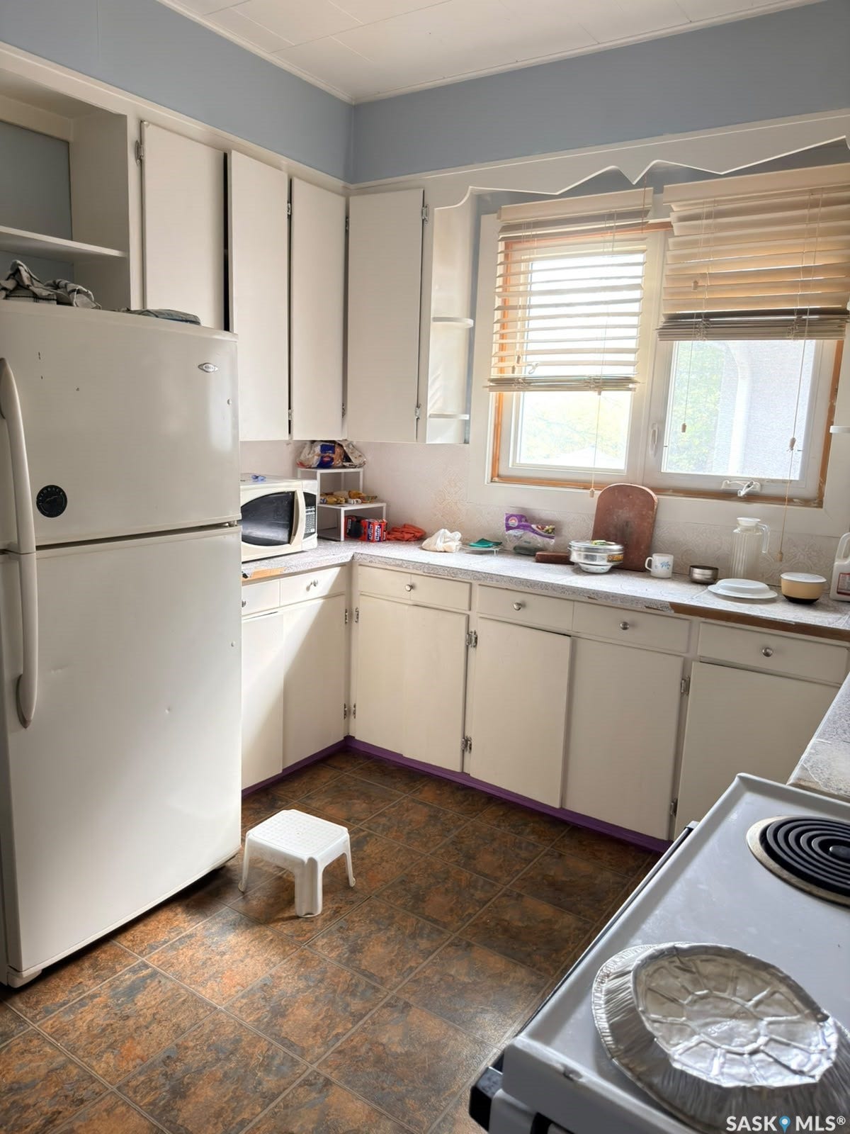 White cabinetry with contrasting wall paint, laminate countertops, and two natural light windows, complemented by a tiled floor