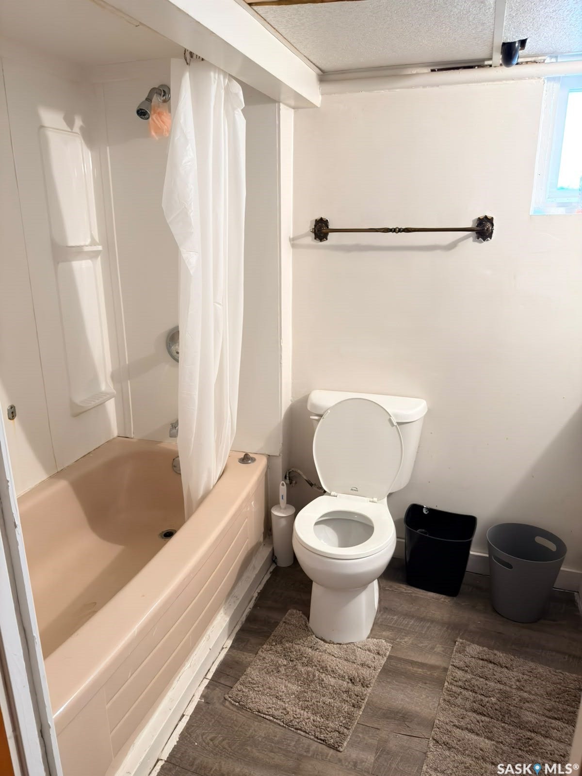 Bathtub with integrated shower, white toilet, and wood-finish flooring