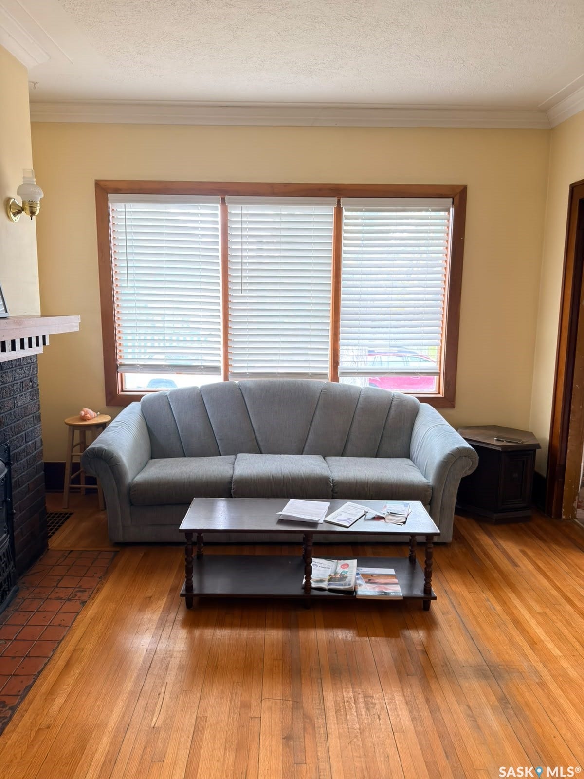 Hardwood flooring throughout, a fireplace with a brick surround, crown molding, and a three-panel window with wood trim