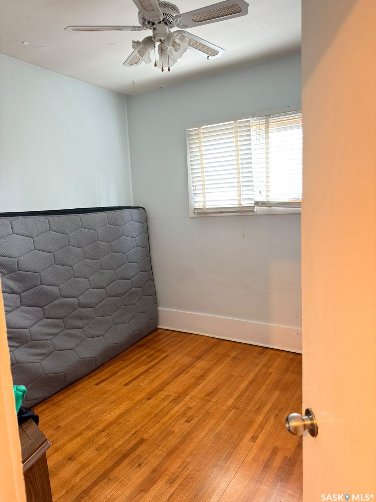 Hardwood flooring, light blue wall paint, ceiling fan light fixture, window with blinds, white trim