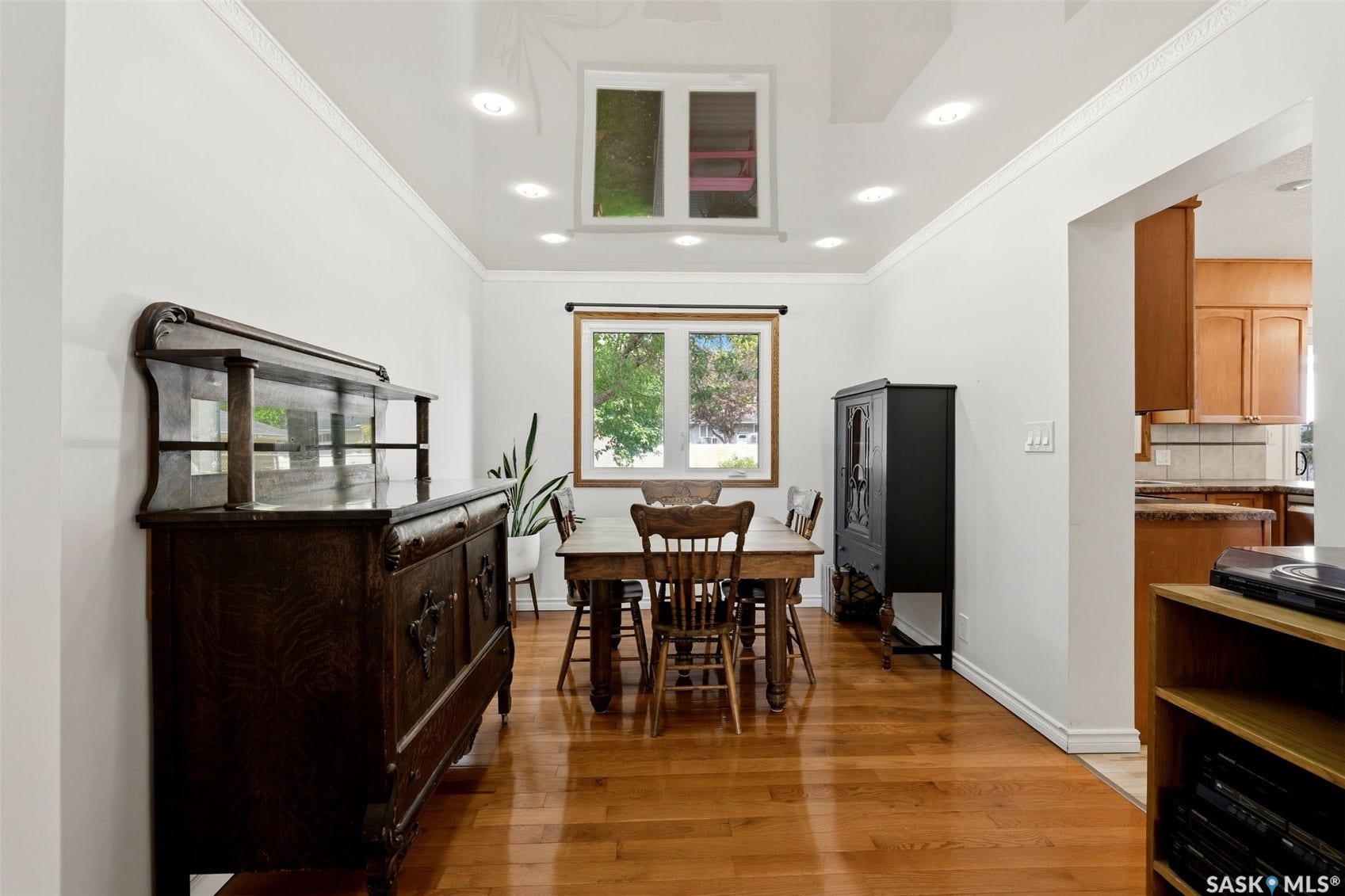 Recessed lighting with a tray ceiling, crown molding, wood-finish flooring, and a kitchen entry