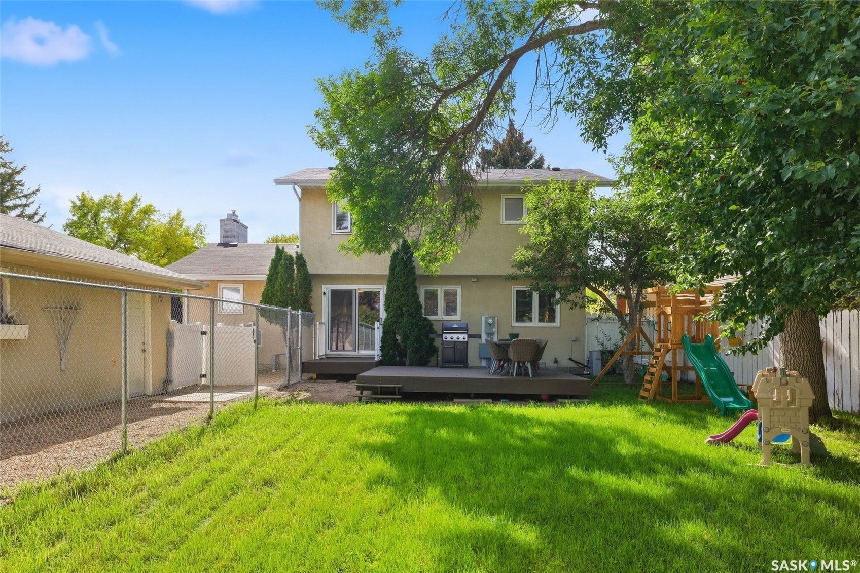 Expansive backyard featuring a manicured lawn, wood-finish deck, and mature trees