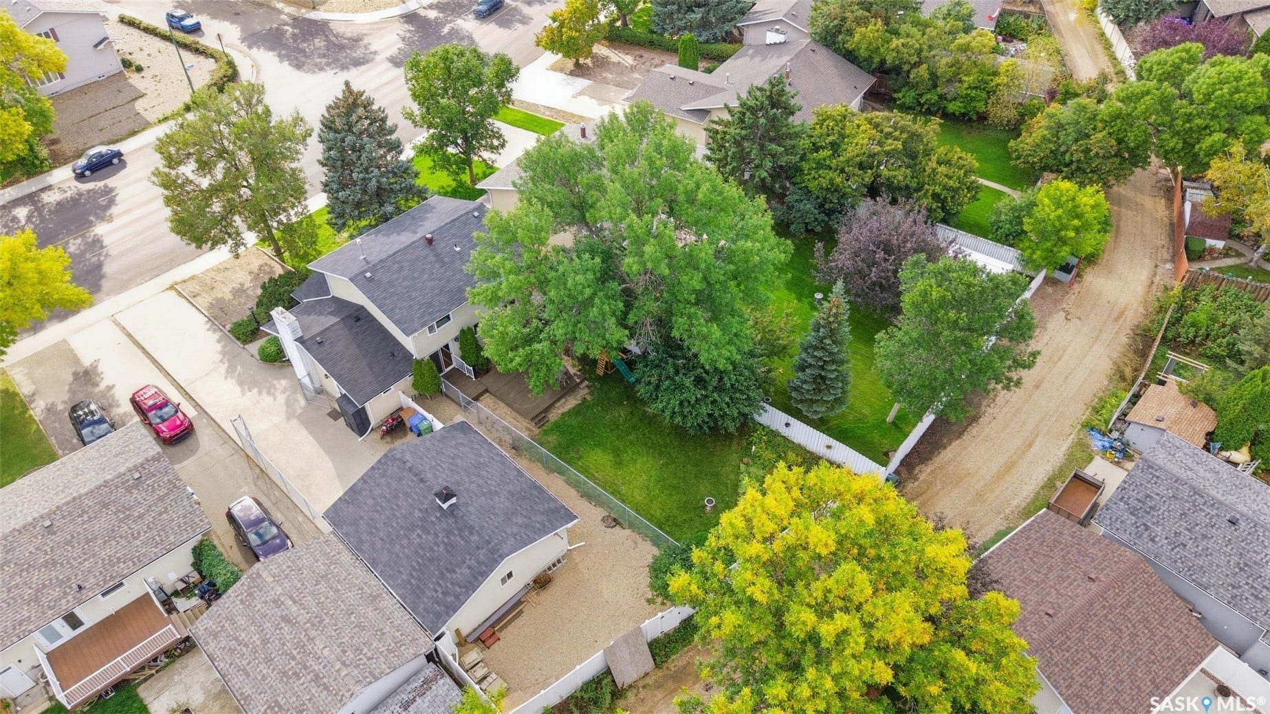 Spacious property featuring a large main residence, detached garage, expansive lawn, mature trees, and paved driveways