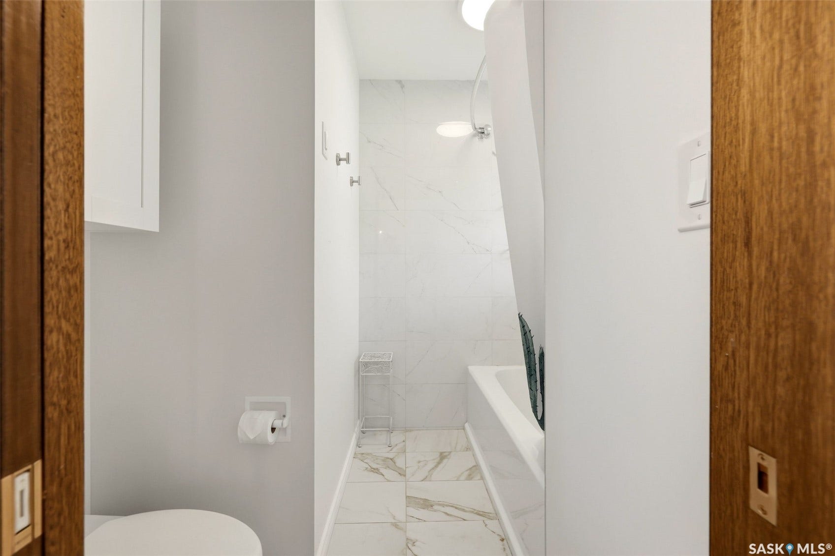 White wall-mounted cabinetry, white toilet, white wall paneling, white bathtub with a shower, and white and gray patterned floor tiling