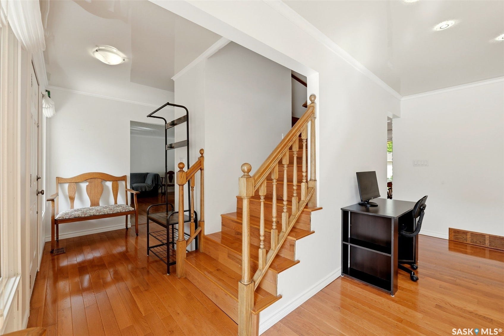 Hardwood flooring throughout, featuring a finished wooden staircase with balusters, crown molding, and recessed lighting