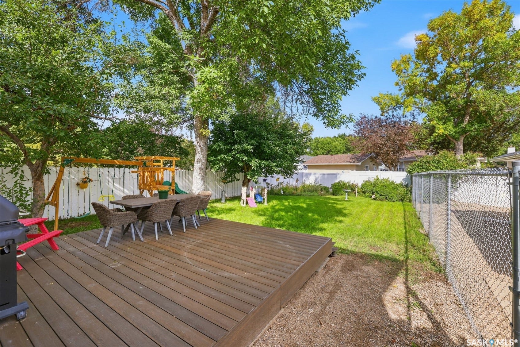 Spacious outdoor deck with a private white fence, mature trees, and a green lawn area
