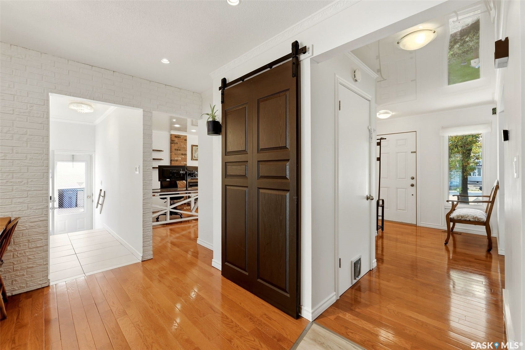 Hardwood flooring, painted brick accent wall, sliding barn door, transom window, and flush-mount lighting
