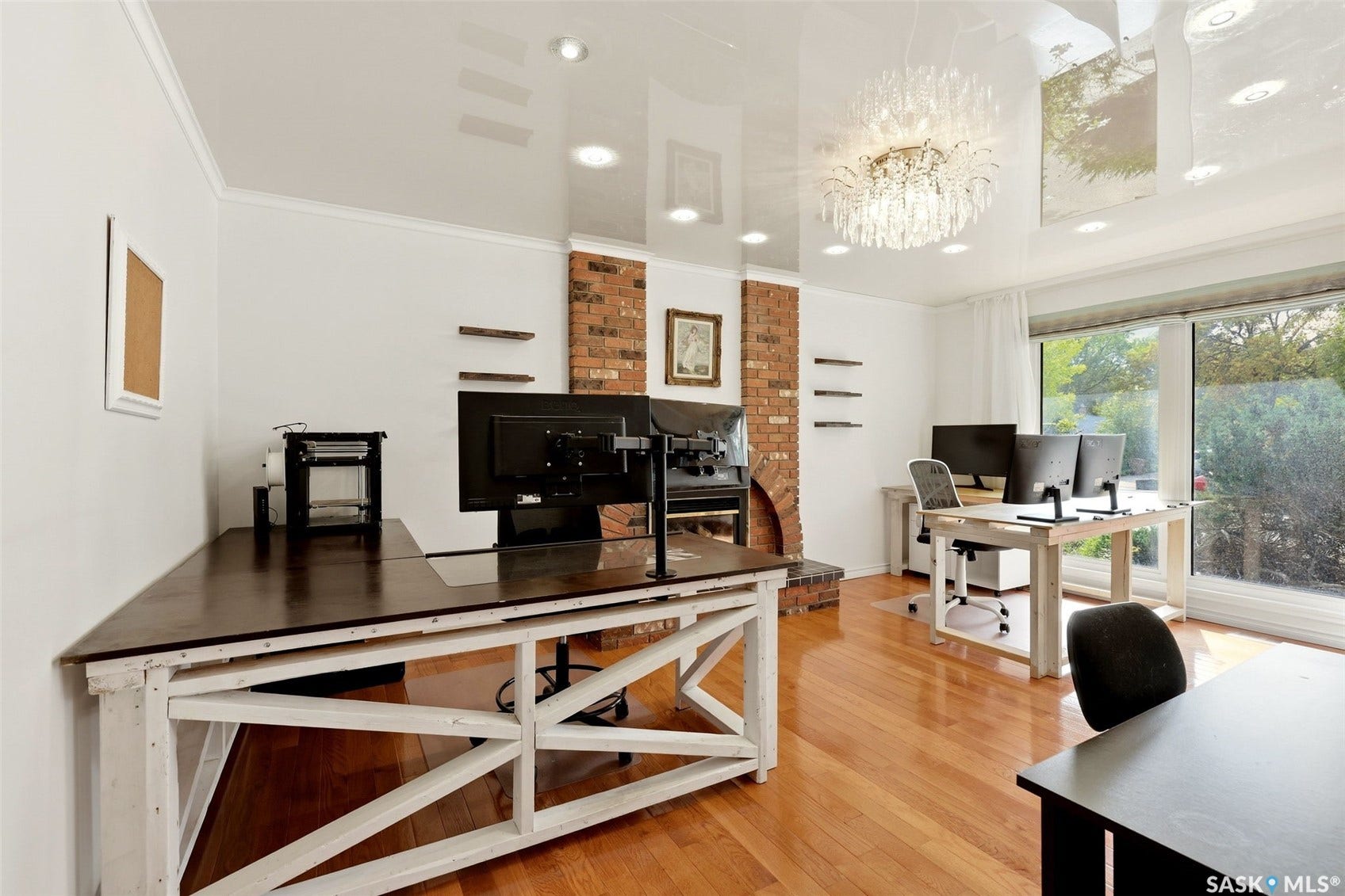 Hardwood flooring throughout, featuring a brick-clad fireplace with a hearth, recessed lighting, and a multi-tiered crystal chandelier