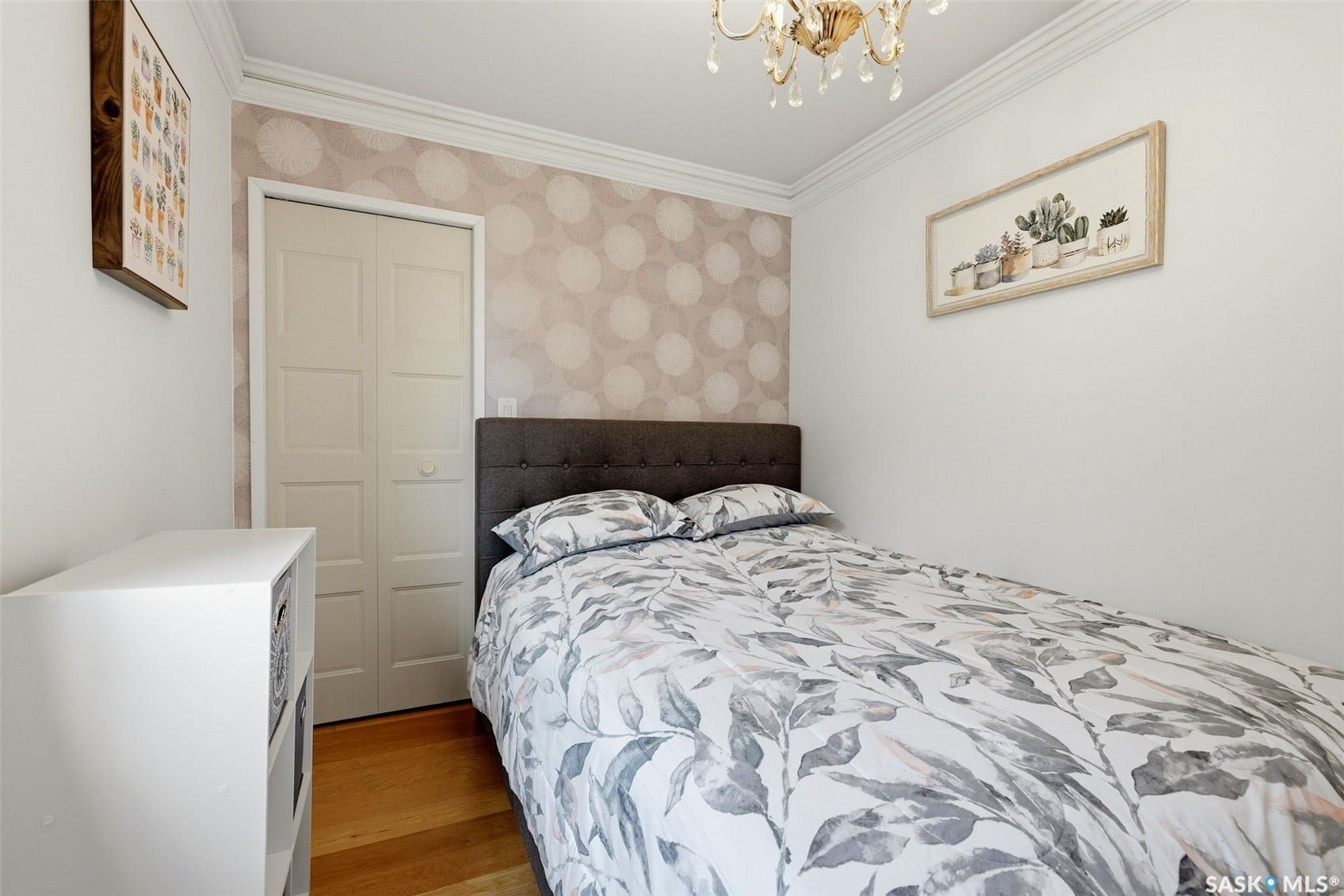 Hardwood flooring, crown molding, patterned accent wall, bi-fold closet doors, and an ornate chandelier