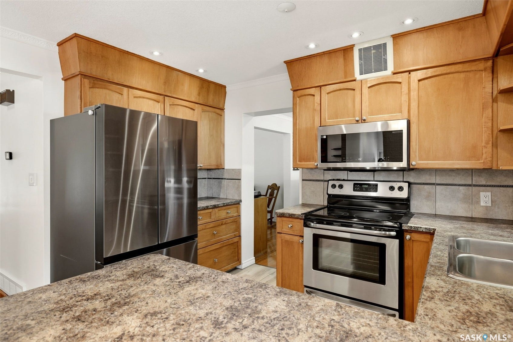 Stainless steel appliances, wood cabinetry, stone-finish countertops, tile backsplash, and recessed lighting