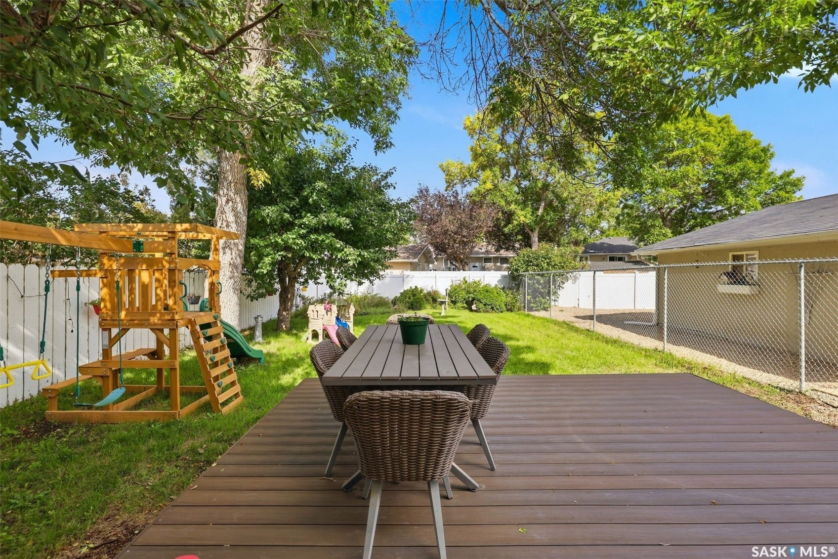 Expansive backyard featuring a composite deck, chain-link fencing, and mature trees