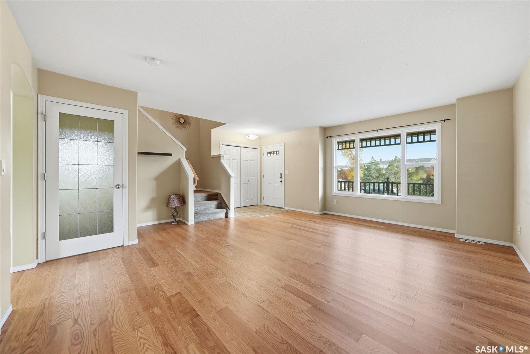 Expansive room with wood-finish flooring, a large multi-pane window, and a carpeted staircase