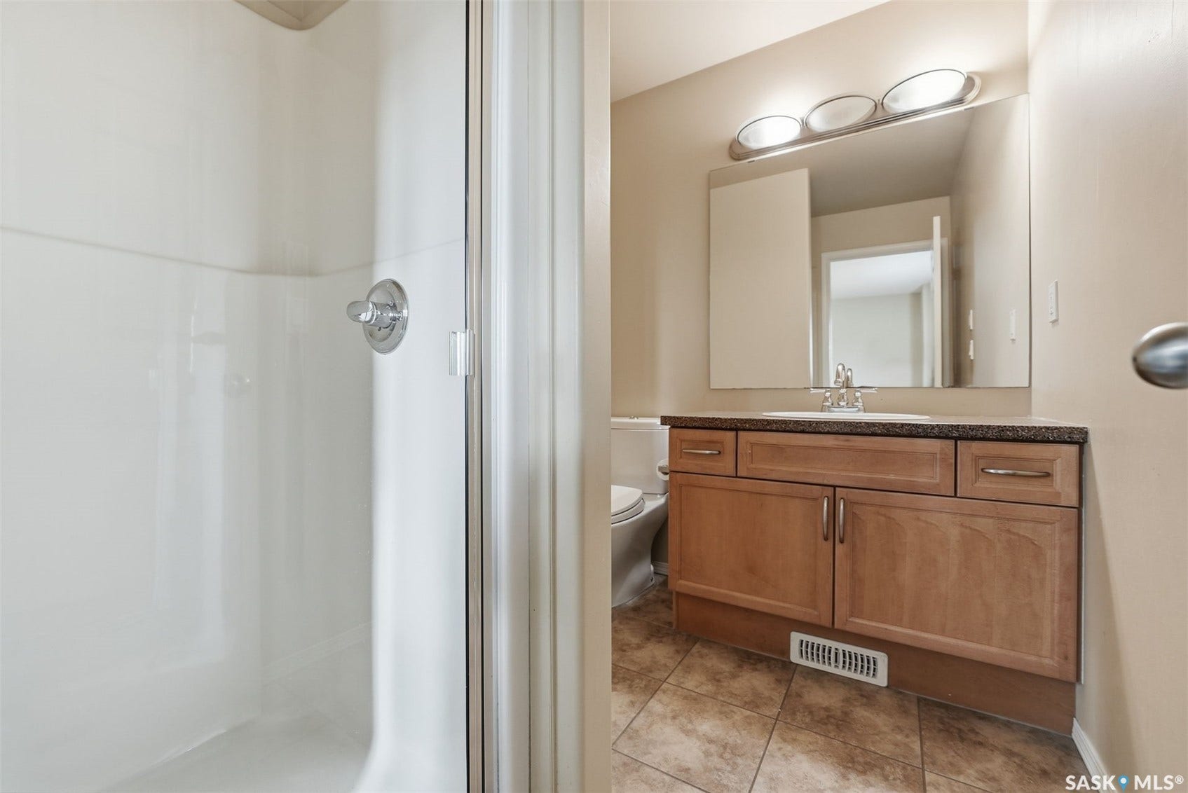 Bathroom featuring a shower with a clear glass enclosure, a single vanity with wood-finish cabinetry, a white drop-in sink, a wall-mounted mirror, and tile flooring