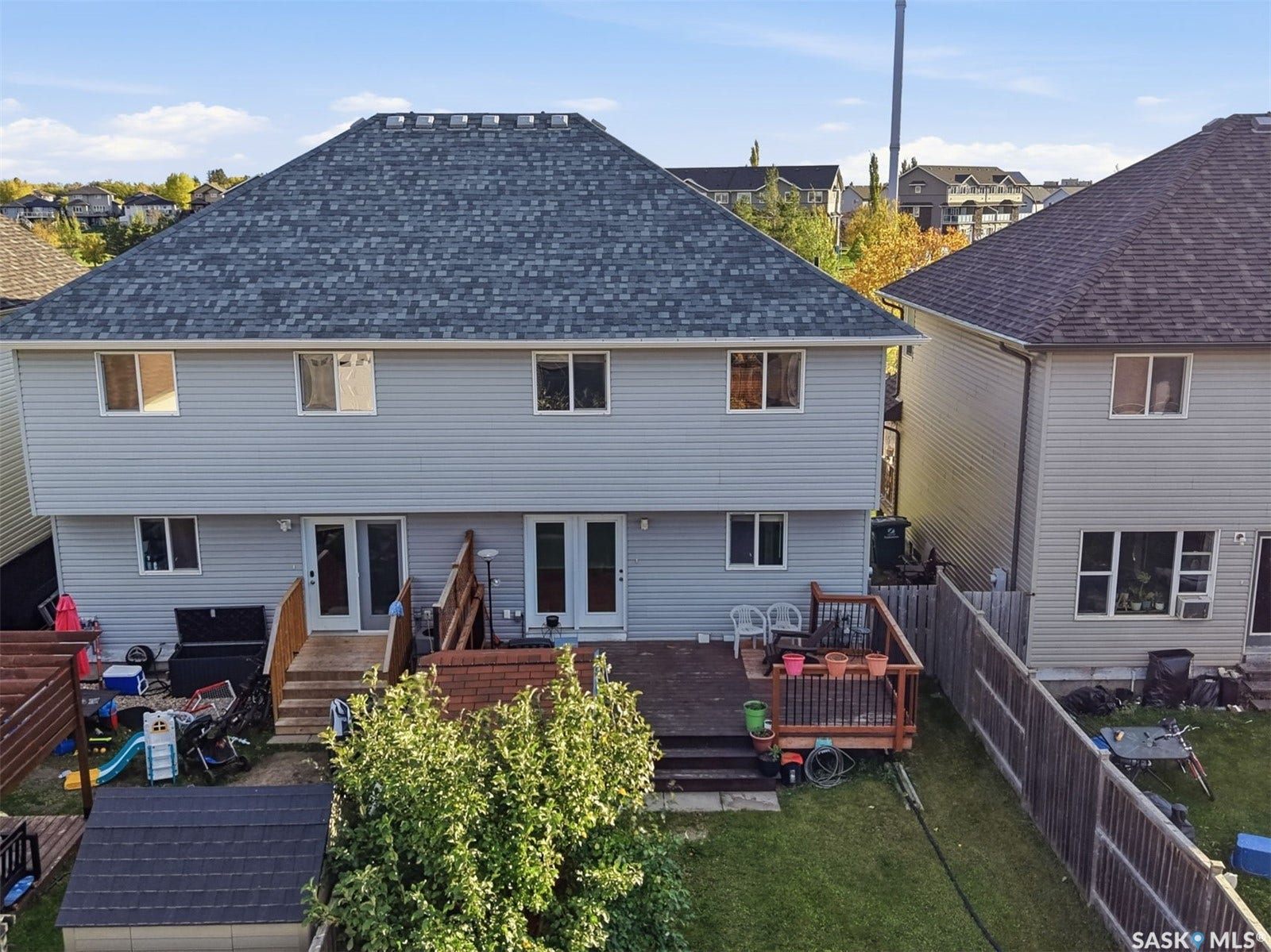 Rear exterior featuring light grey siding, a wood deck with railings, and a shingled roof