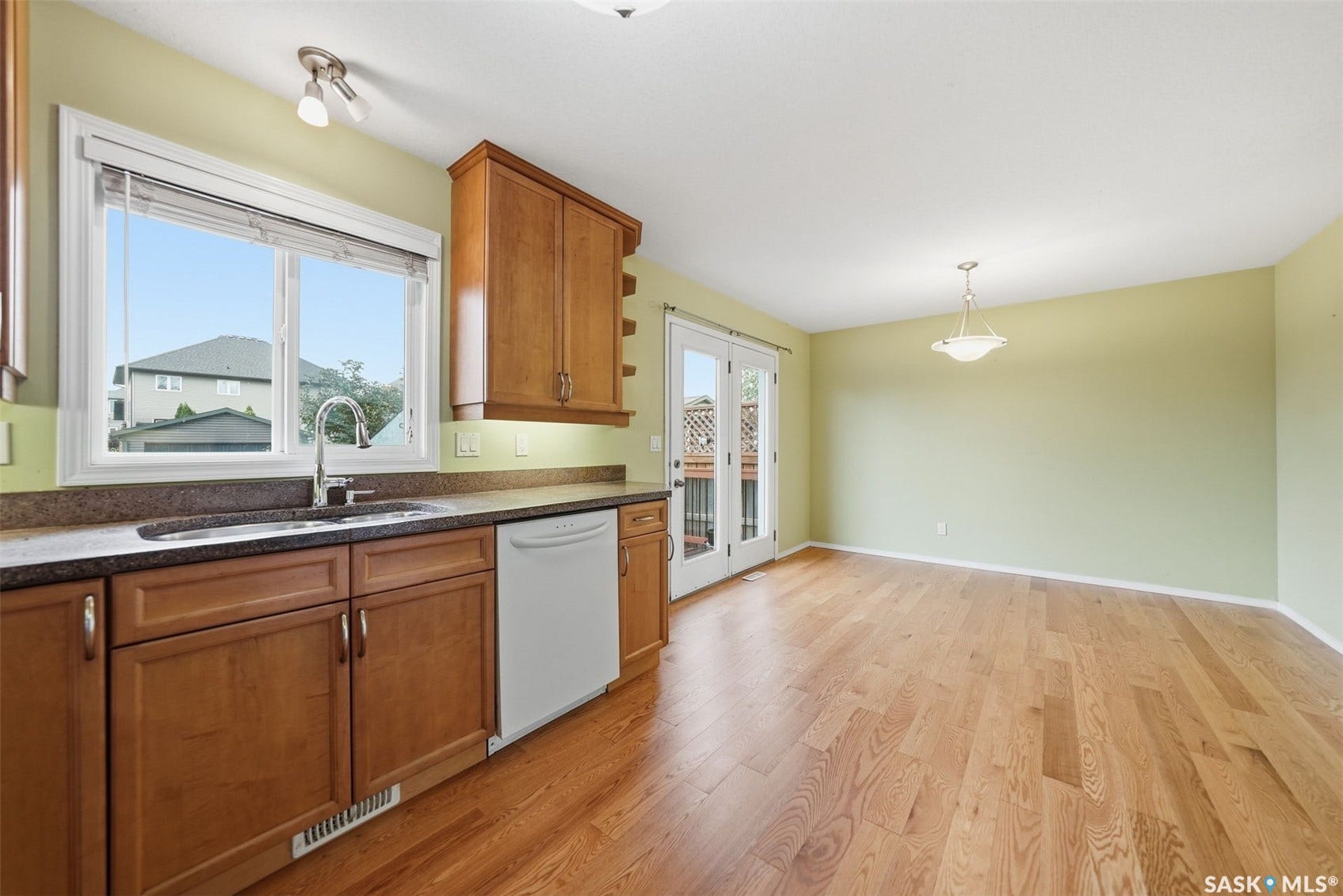 Wood-finish flooring, wood cabinetry, built-in dishwasher, dual basin sink with gooseneck faucet, and double French doors with external deck access