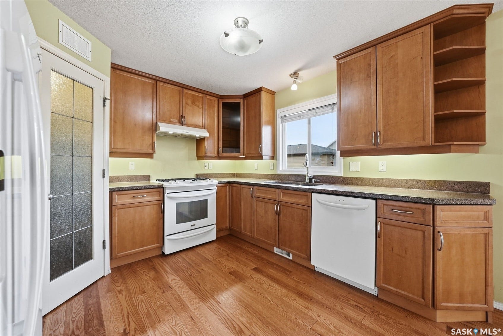 Kitchen featuring wood-finish flooring, wood cabinetry, stone-finish countertops, a gas range, and a built-in dishwasher