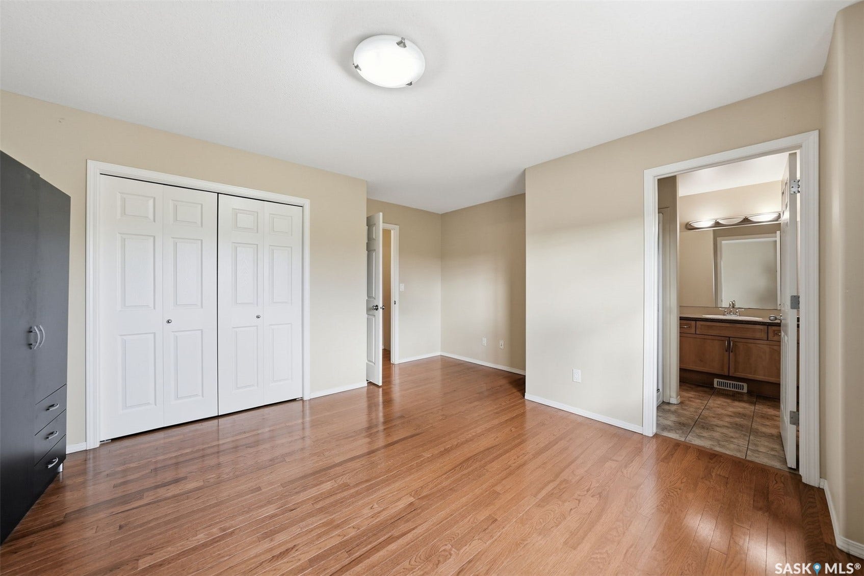 Warm wood-finish flooring throughout, featuring a double-door closet with white paneled doors, and a ceiling-mounted flush light fixture