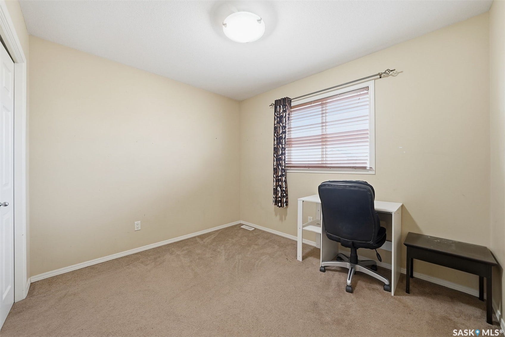 Carpeted room with a ceiling-mounted light fixture and a window with blinds
