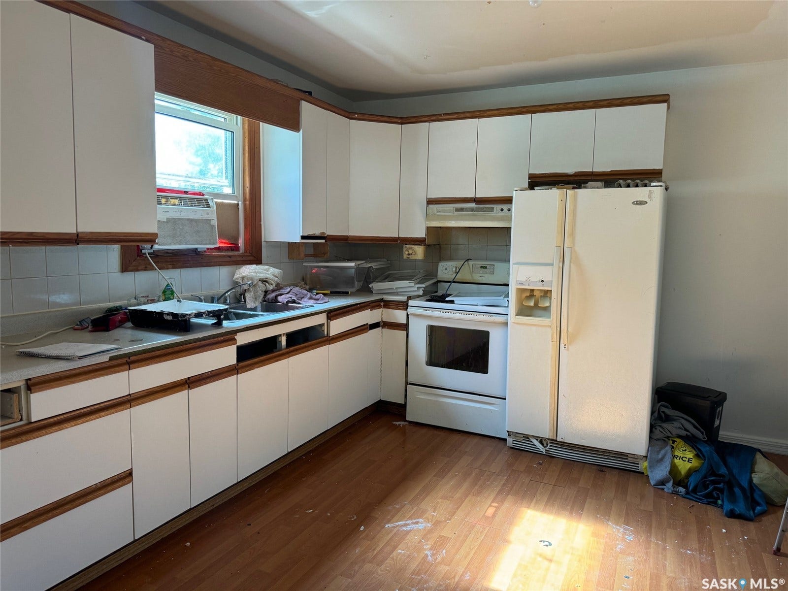 Kitchen with wood-finish flooring, white cabinetry with wood trim, white tile backsplash, and a window above the sink
