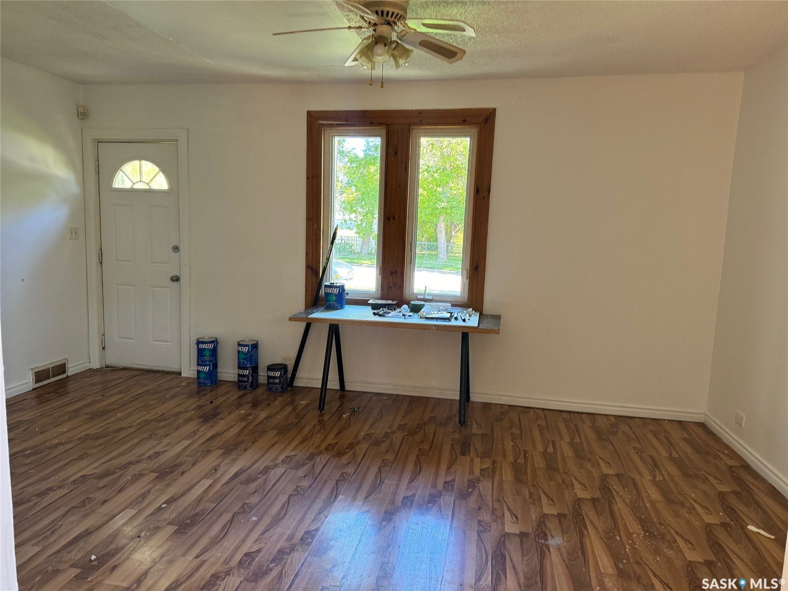 Bright and spacious living area featuring newly installed wood-finish flooring, a ceiling fan with integrated lighting, and dual glass doors with wooden frames that frame natural outdoor light