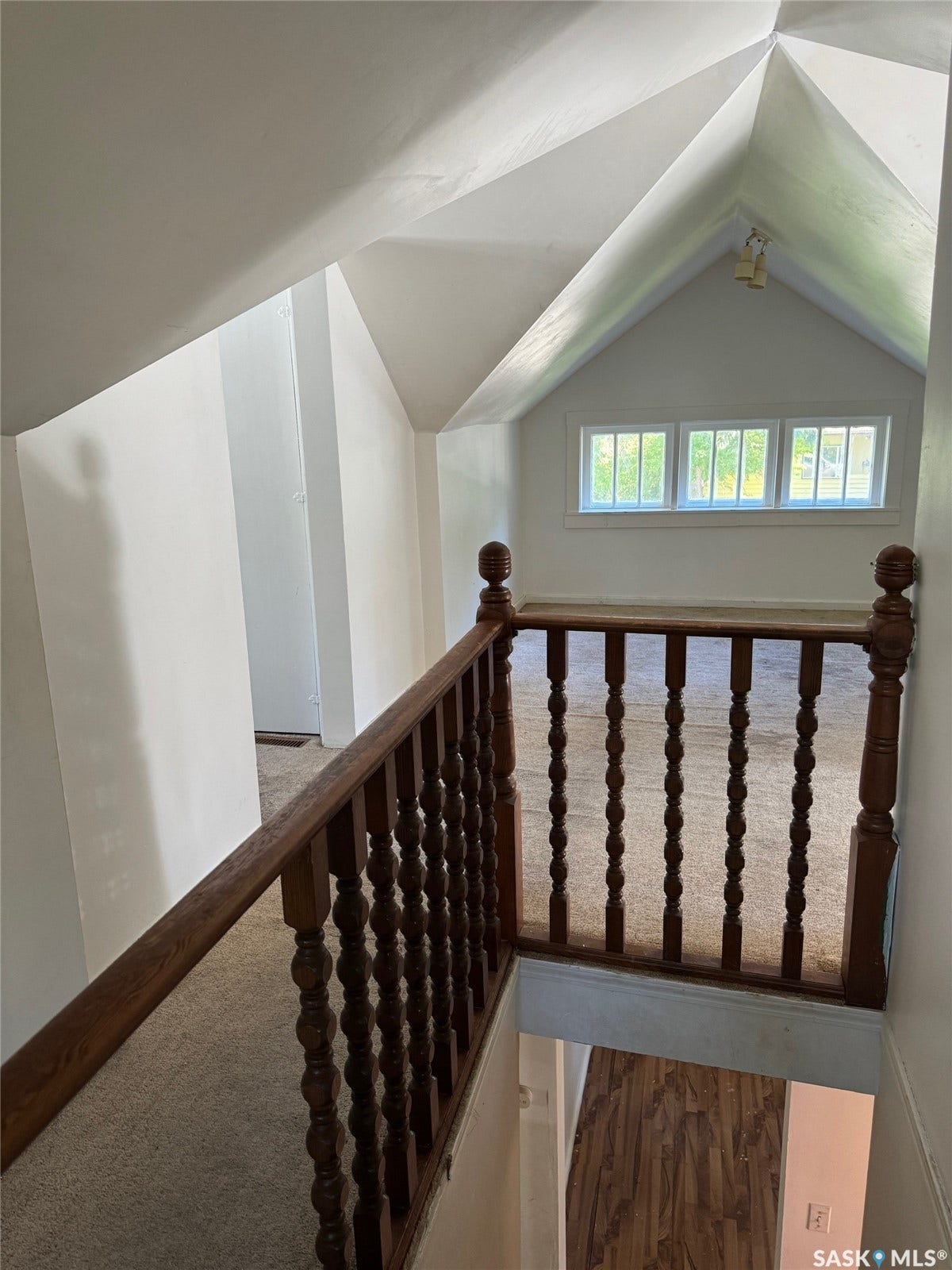 Elegant upper-level landing featuring turned wood balustrade railing, peaked ceiling with transom window, and abundant natural light from multi-pane fenestration
