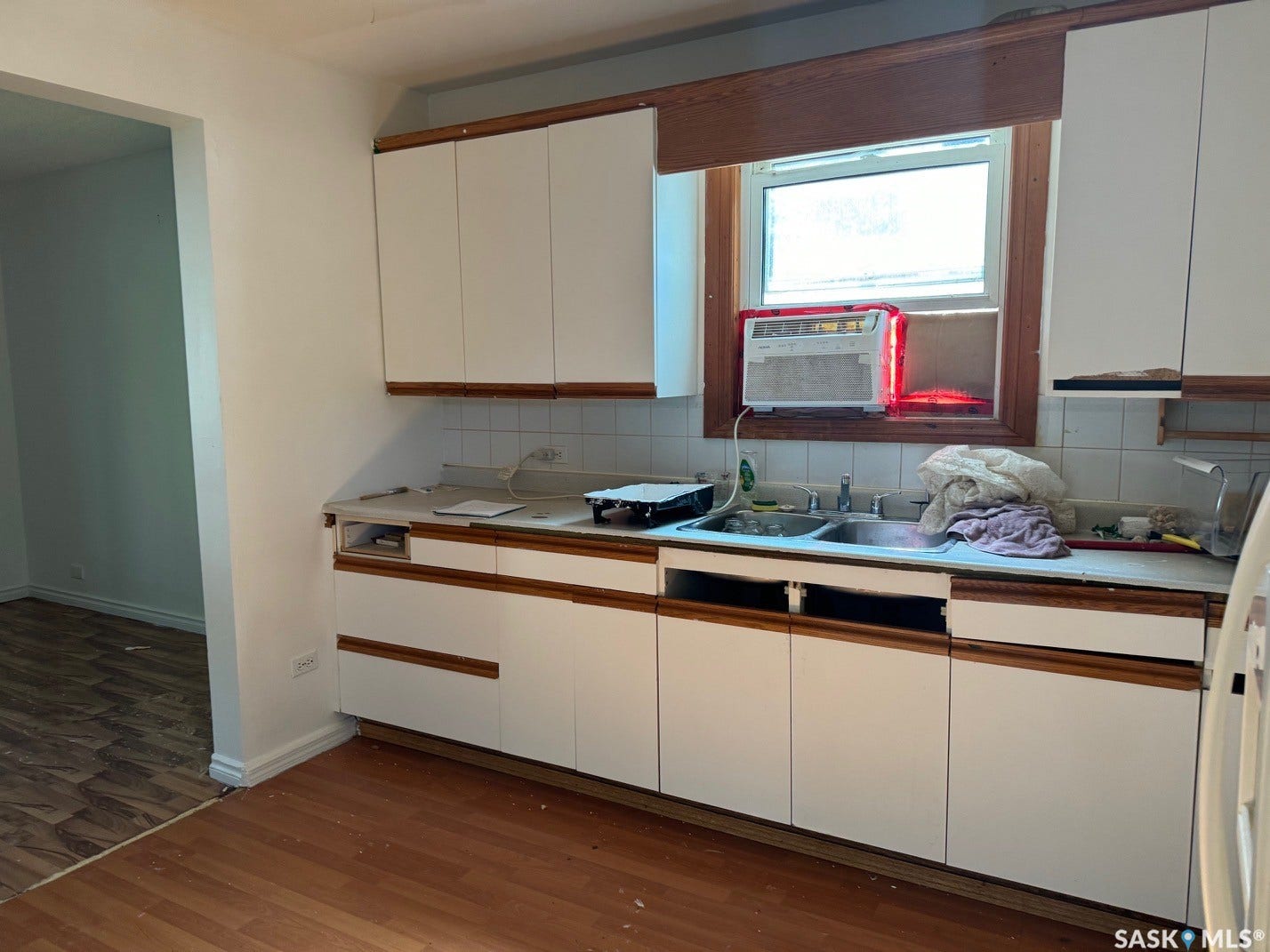White cabinetry with wood trim, double basin sink, white tile backsplash, and wood-finish flooring