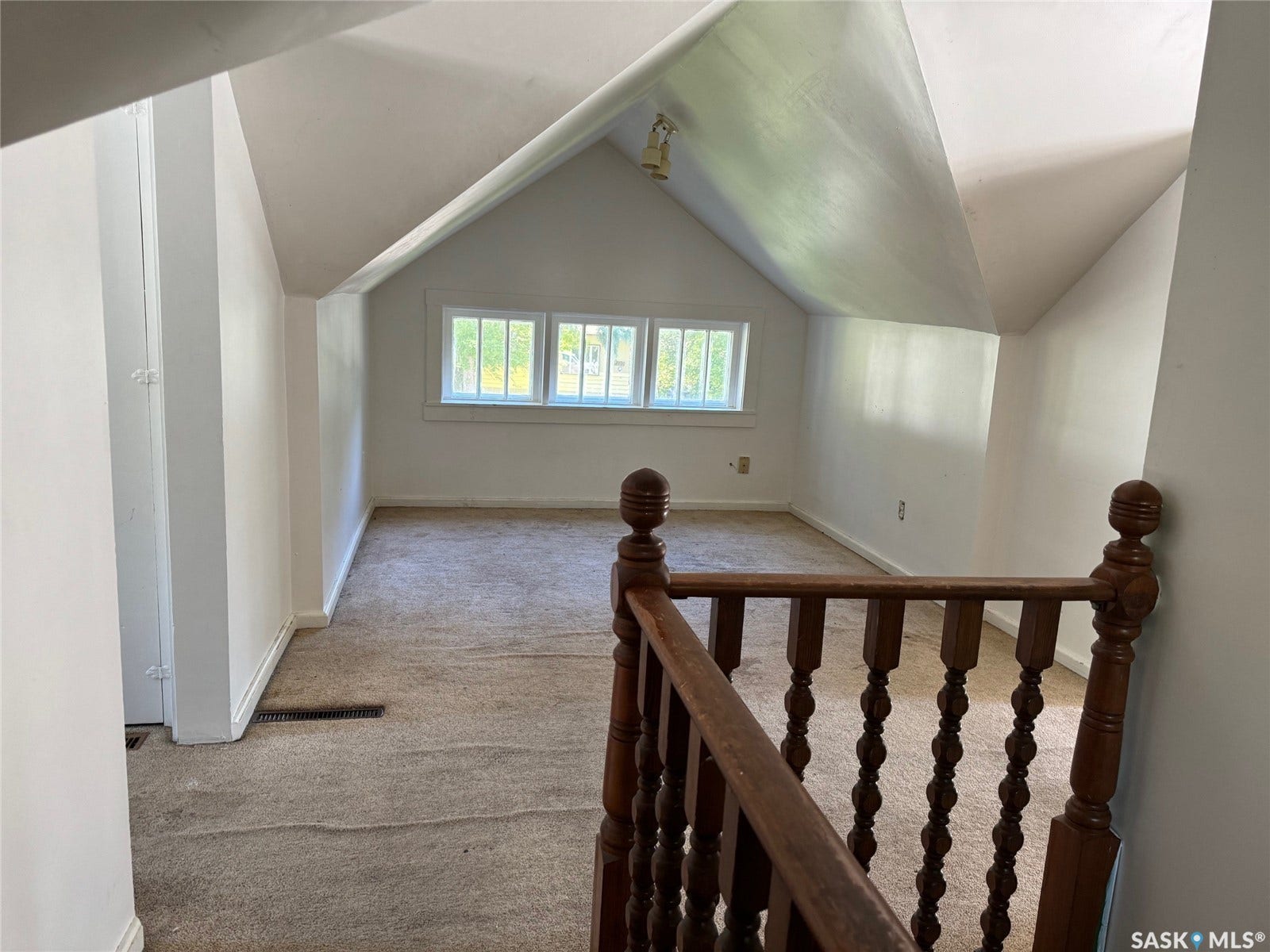 Bright upper-level room with vaulted ceilings, transom windows providing natural light, wood-finish railing, and carpeted flooring throughout