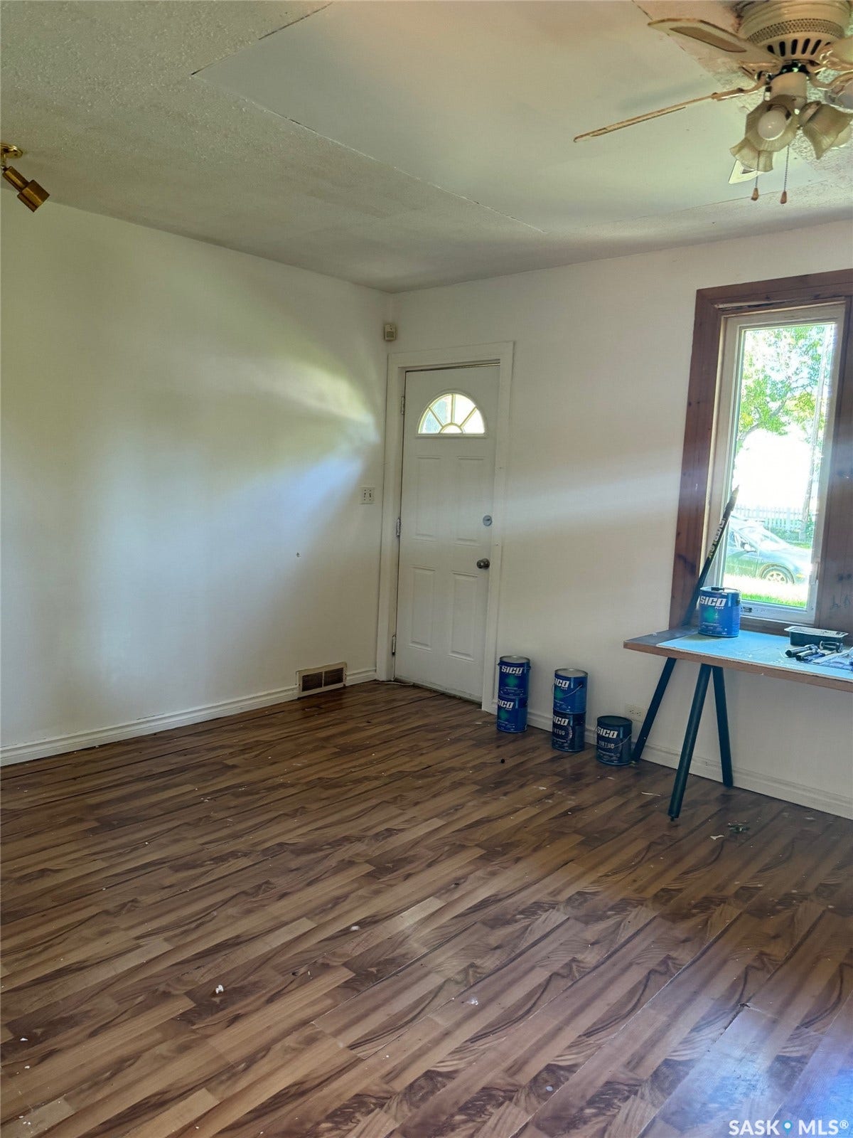 Bright, open living space featuring wood-finish flooring throughout, natural light from multiple windows, ceiling fan with integrated lighting, and a clear floor plan ideal for flexible use