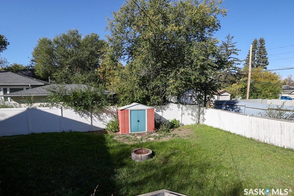 Expansive yard featuring a manicured lawn, white privacy fencing, and a red and blue storage shed